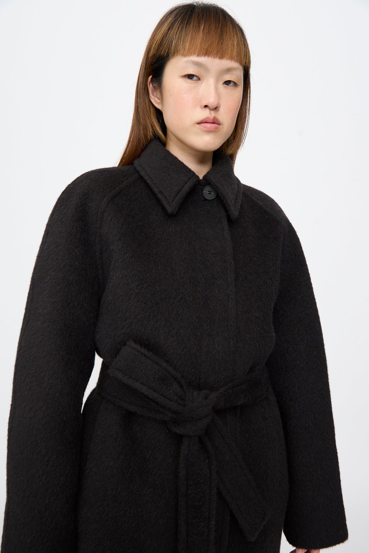 Studio Nicholson Mohair Kober Coat in Cola: a dark brown, oversized virgin wool coat with a textured finish, a collar, and a tie-waist belt.