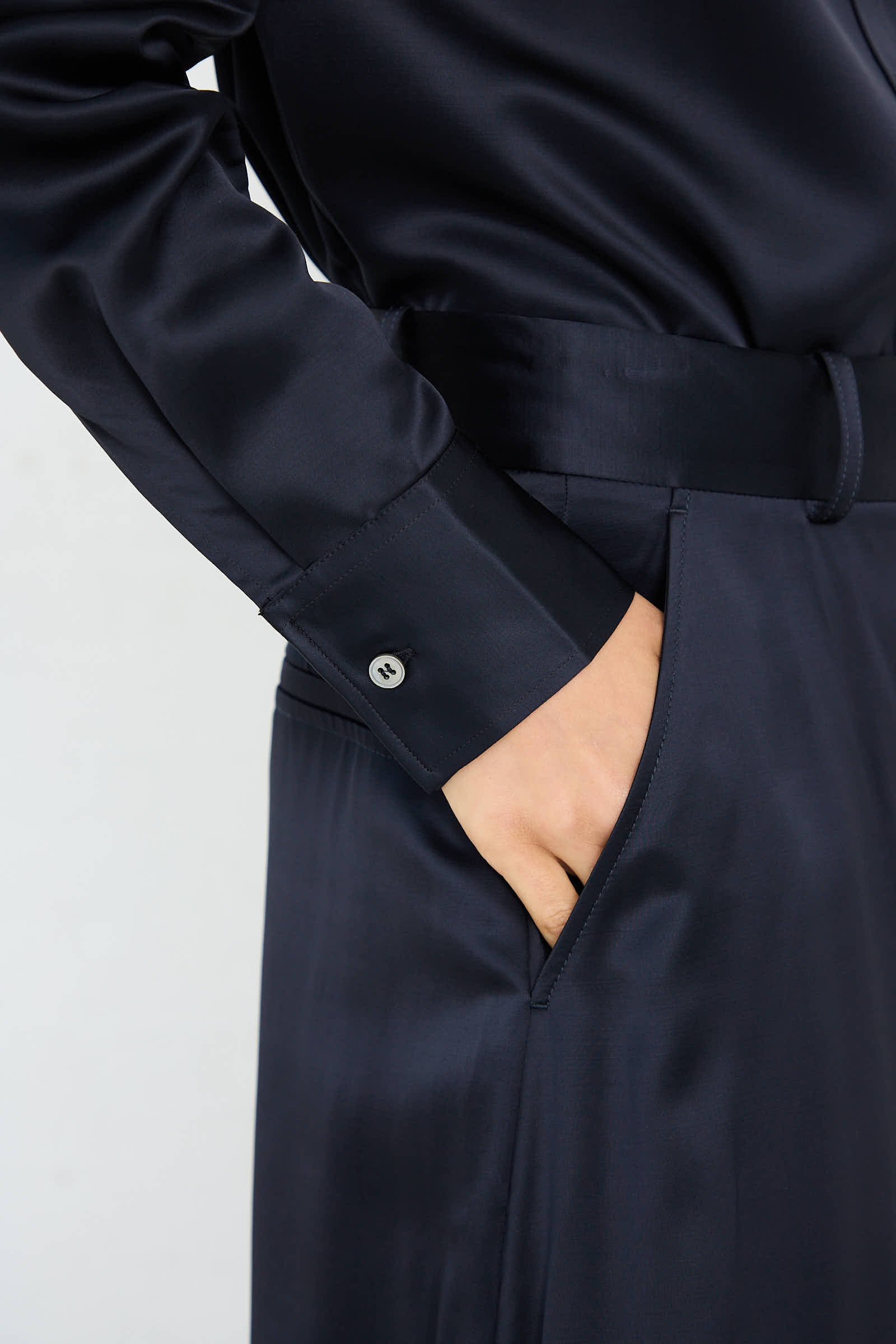 Close-up of a person wearing a dark silk garment with a collared sleeve and a belt, placing their hand into the side pocket of their high-rise Myers Pant in Black Ink by Studio Nicholson.