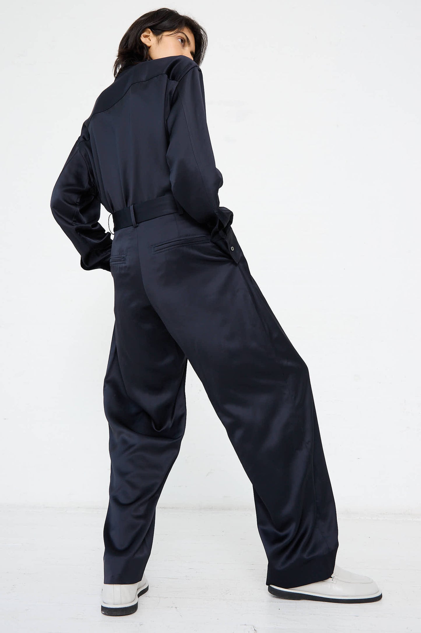 A person wearing the Myers Pant in Black Ink by Studio Nicholson and white shoes is shown from the back, standing against a plain white background.