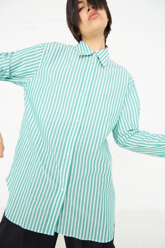 A person in a Studio Nicholson Santos Overshirt in Green and Cream standing against a white background, with one arm extended to the side.