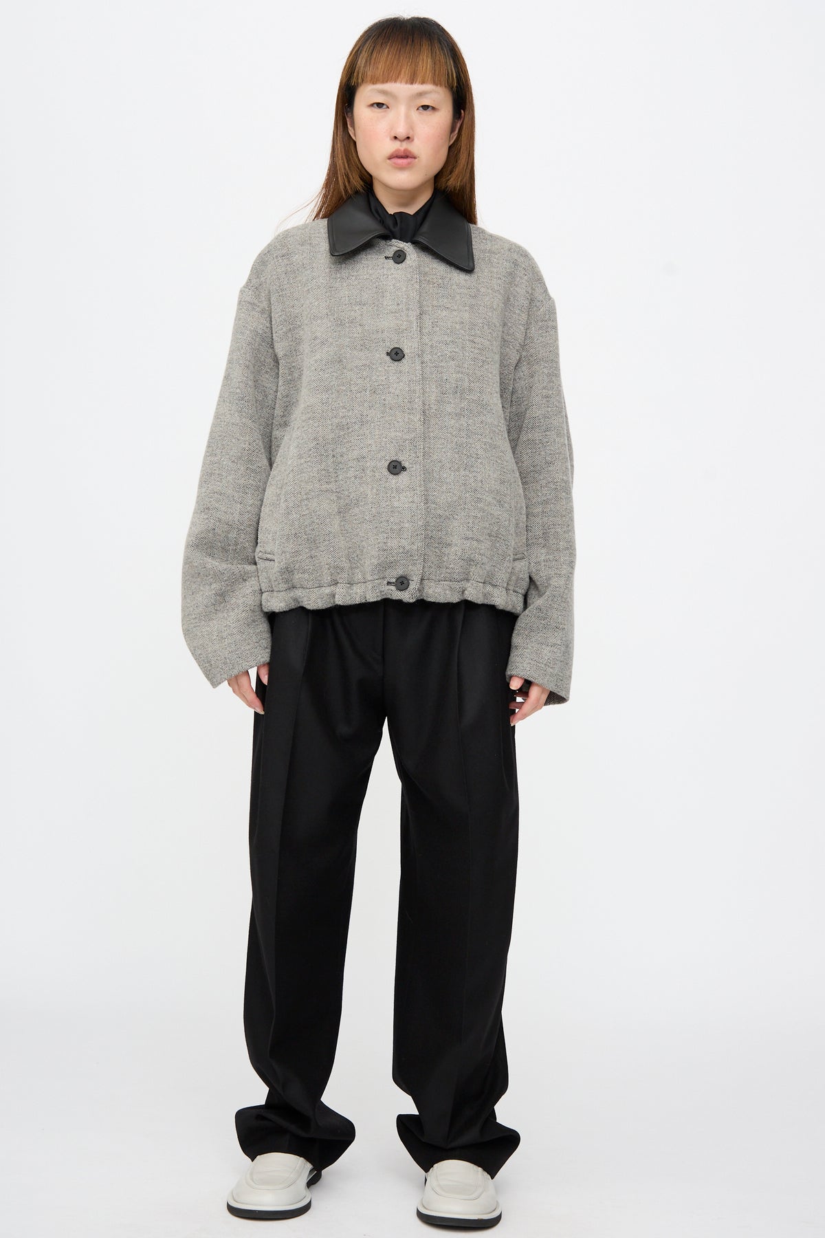A person wearing a Studio Nicholson Seberg Chore Jacket in Black and White with a black collar over black trousers and white shoes.