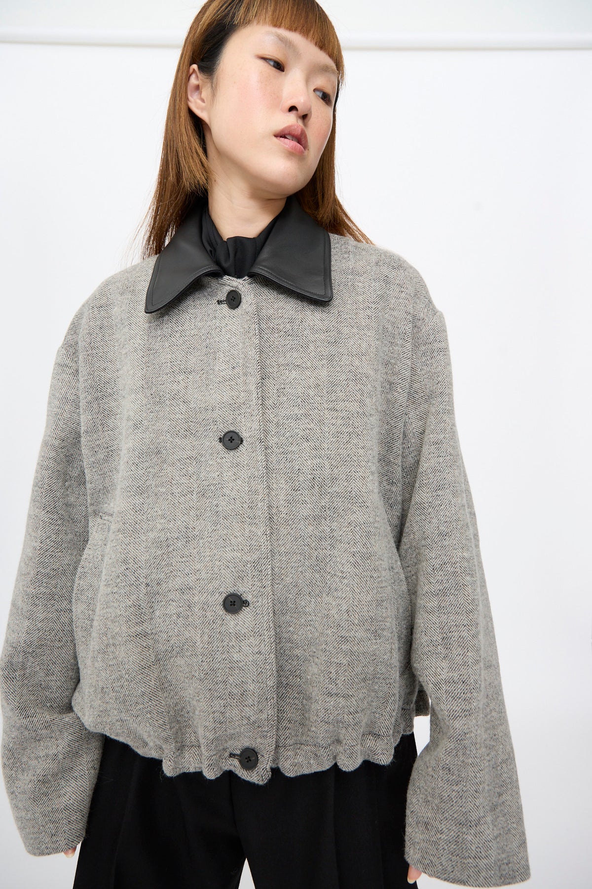 A person wearing a Studio Nicholson Seberg Chore Jacket in Black and White, featuring a dark, pointed leather collar and front button closure.