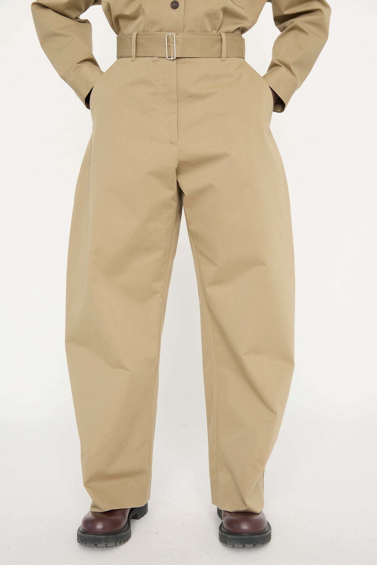 A model in the Studio Nicholson Soft Technical Twill Doring Pant in Parcel, featuring tailored pants and hands in pockets, shows only the torso and legs against a white backdrop. 