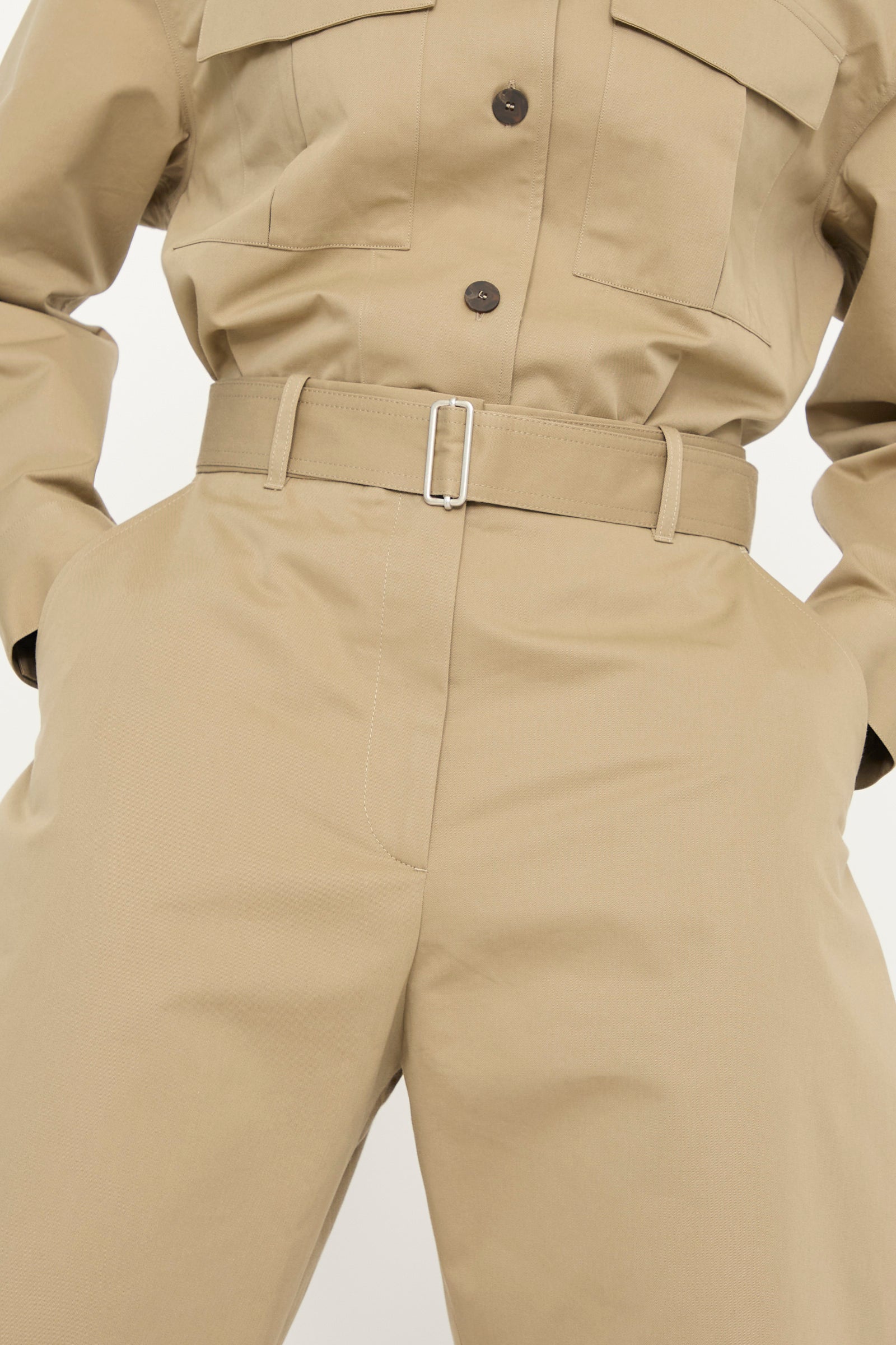 A person models the Studio Nicholson Soft Technical Twill Doring Pant in Parcel, featuring a tan belted design with buttoned pockets and a high waist, shown against a plain background.