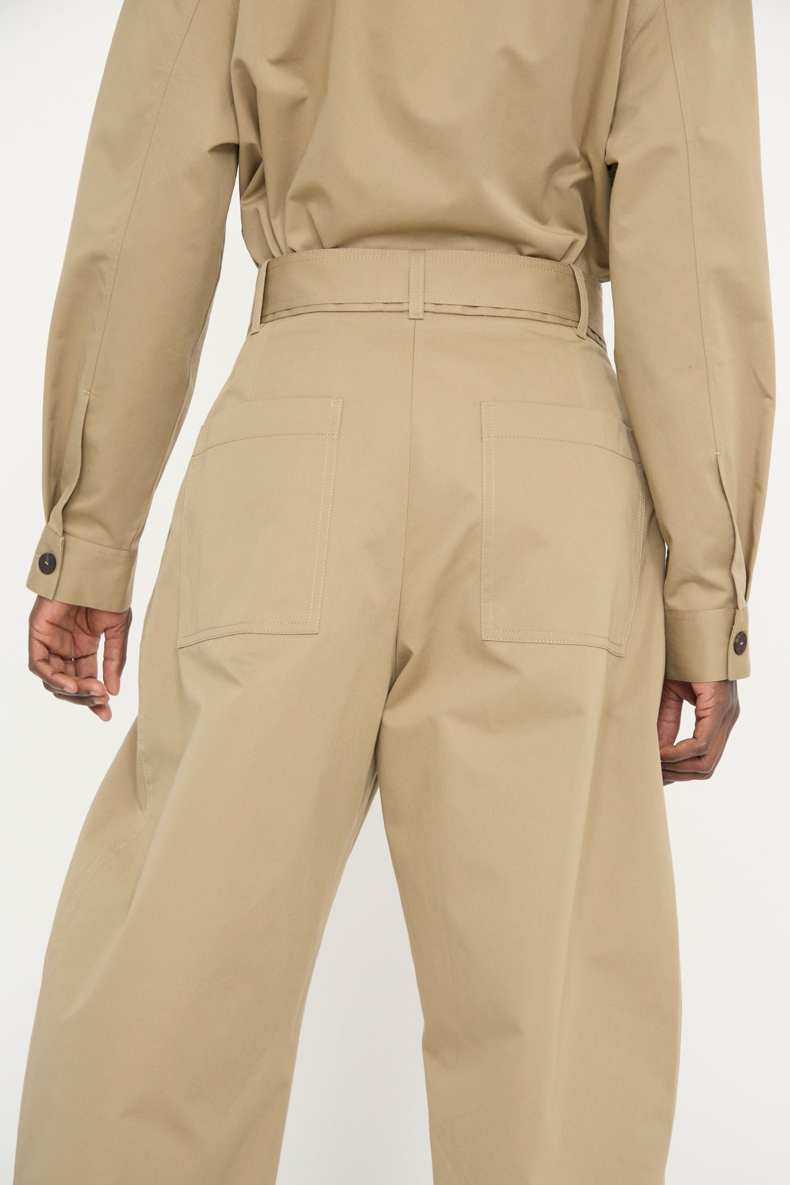 A person is wearing a beige ensemble, seen from the back, featuring Studio Nicholson's Soft Technical Twill Doring Pant in Parcel with a high waist, long sleeves, and wide-leg pants.