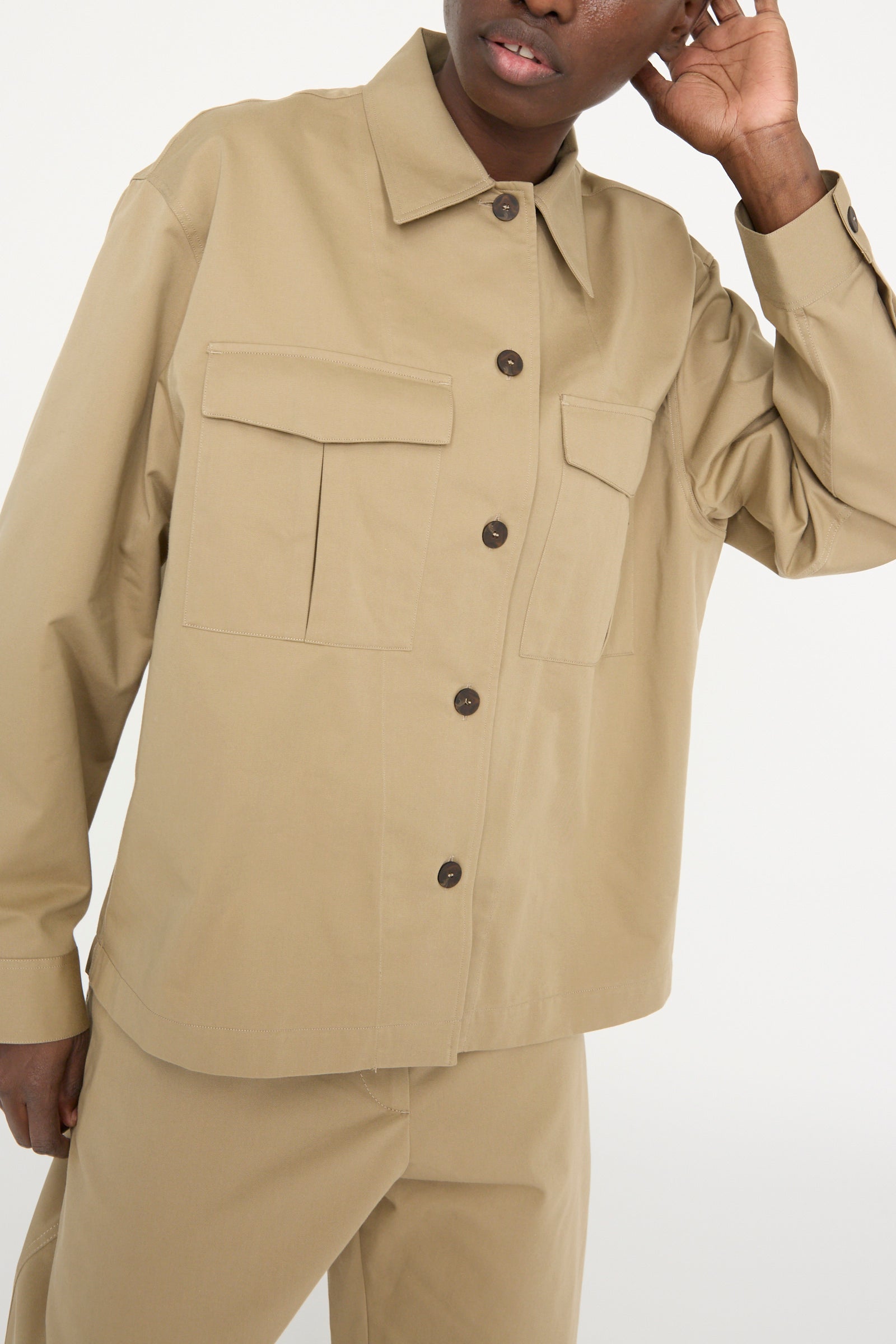 A person wearing the Studio Nicholson Soft Technical Twill Kukes Over Shirt in Parcel, showcasing large front pockets and matching pants against a white backdrop.