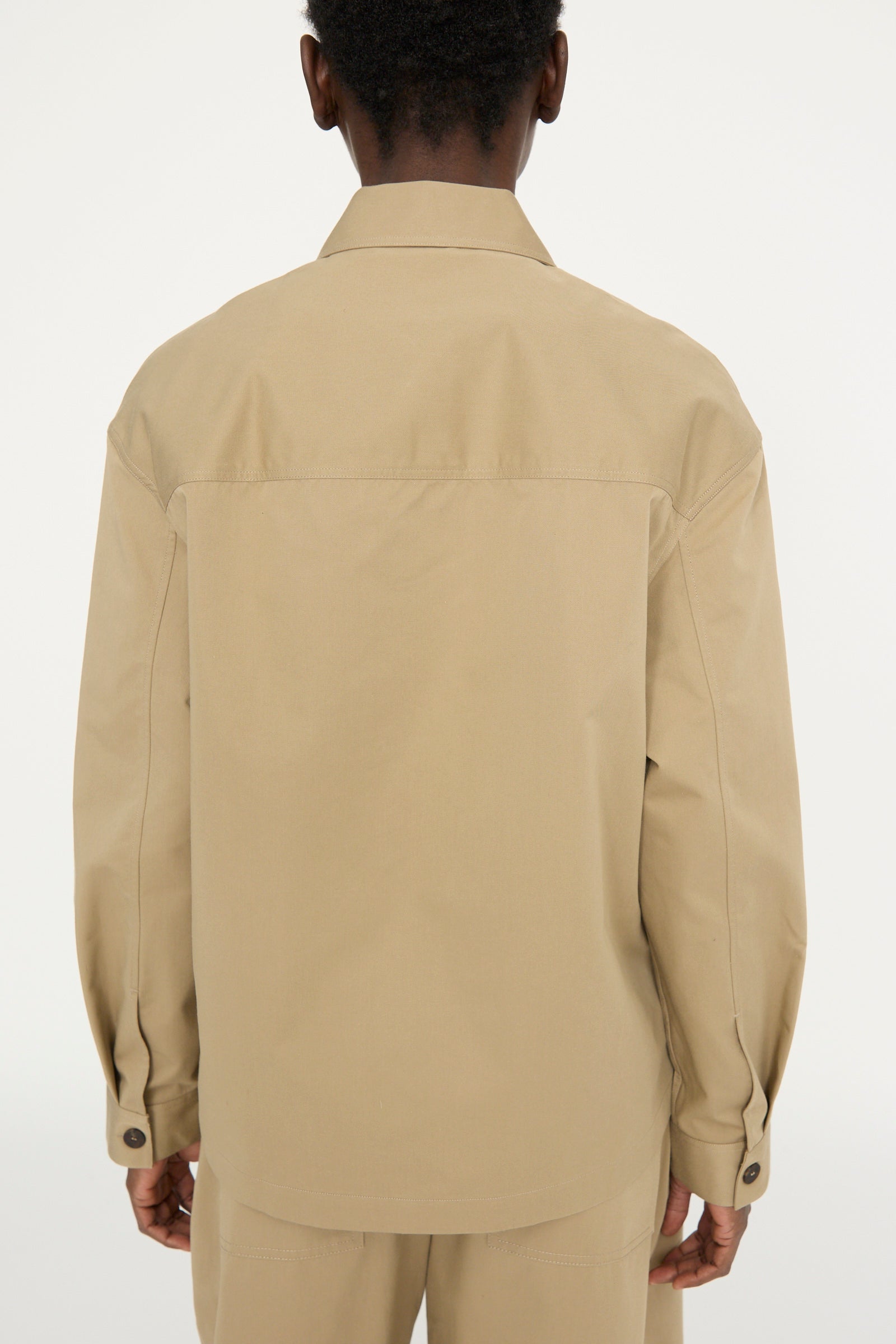 A person is wearing the Soft Technical Twill Kukes Over Shirt in Parcel by Studio Nicholson with matching pants, viewed from the back against a plain white background. 