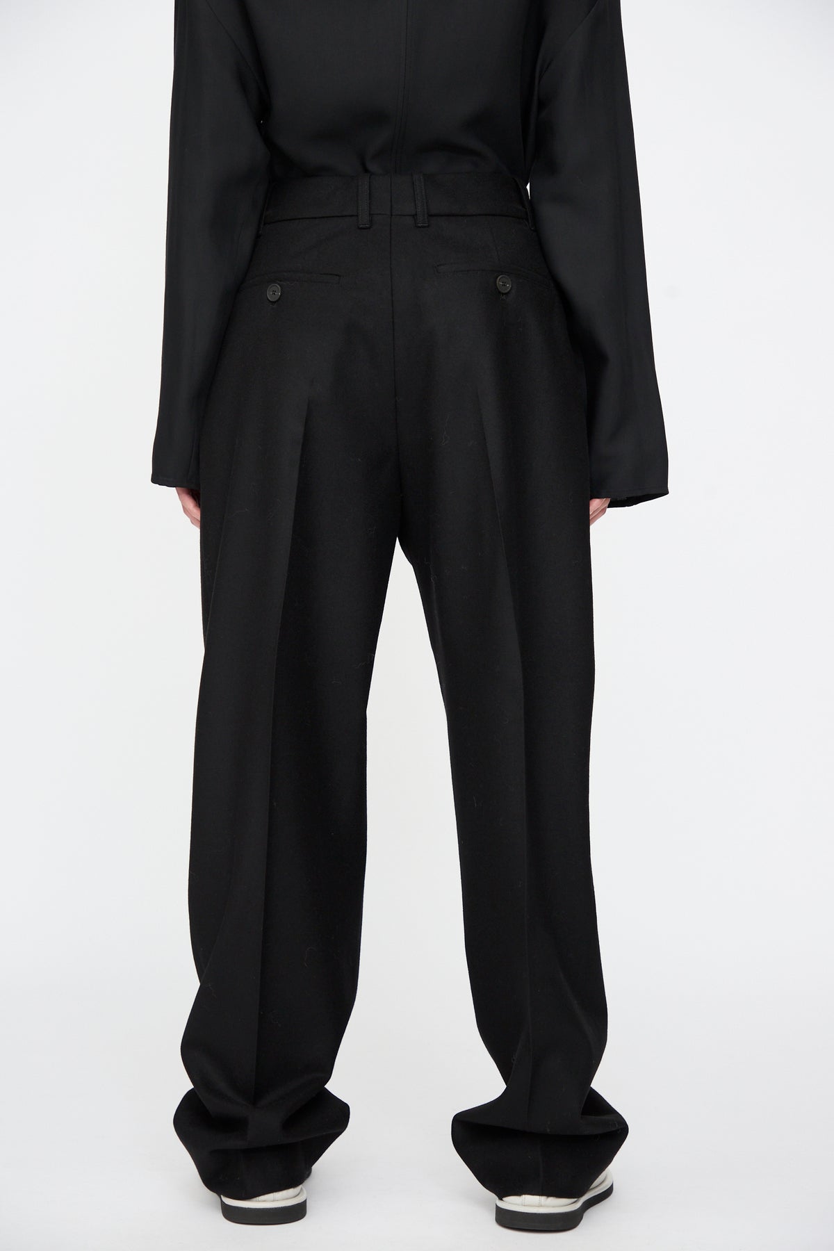 Back view of black Studio Nicholson Sperro Double Pleat Pant with a wide-leg fit, double pleats at the waist, and two buttoned back pockets.