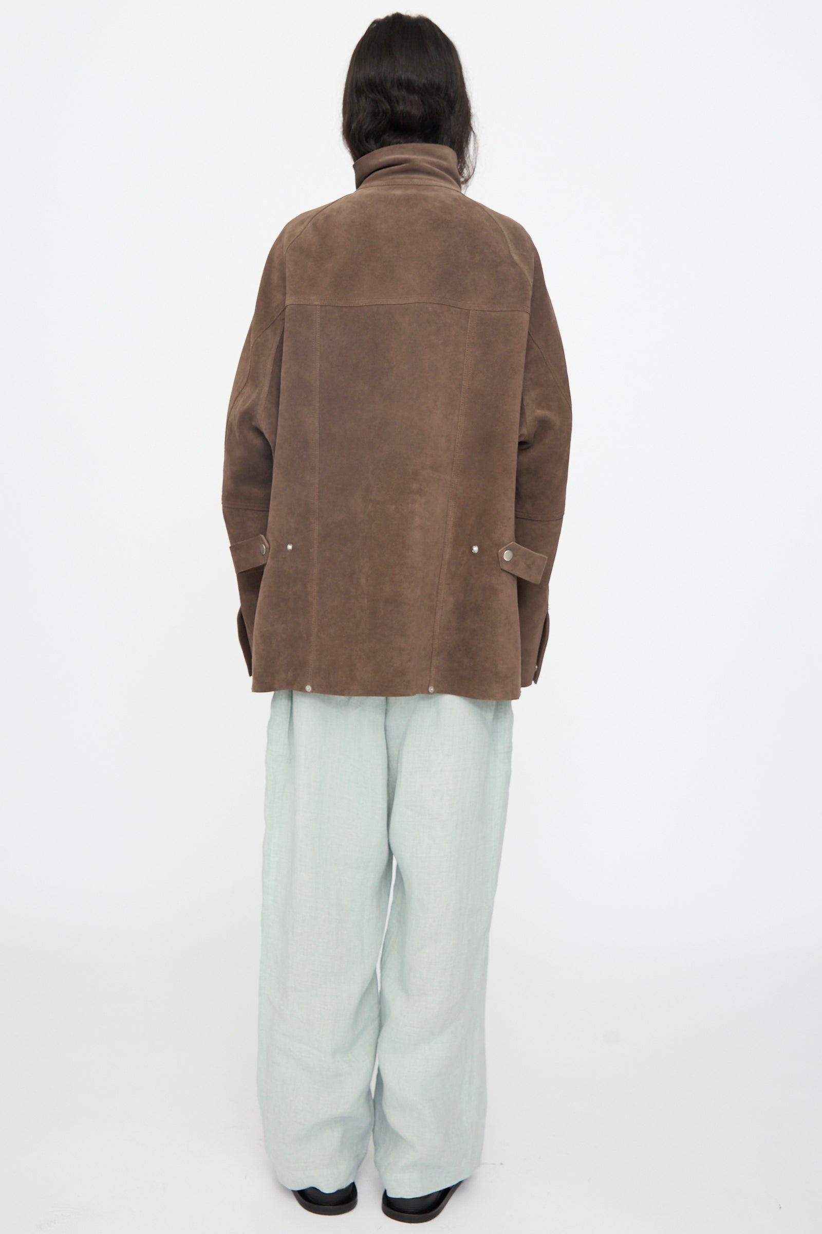 Person facing away, wearing Studio Nicholson's Suede Utility Dash Jacket in Grey and loose light gray pants, set against a plain white background.