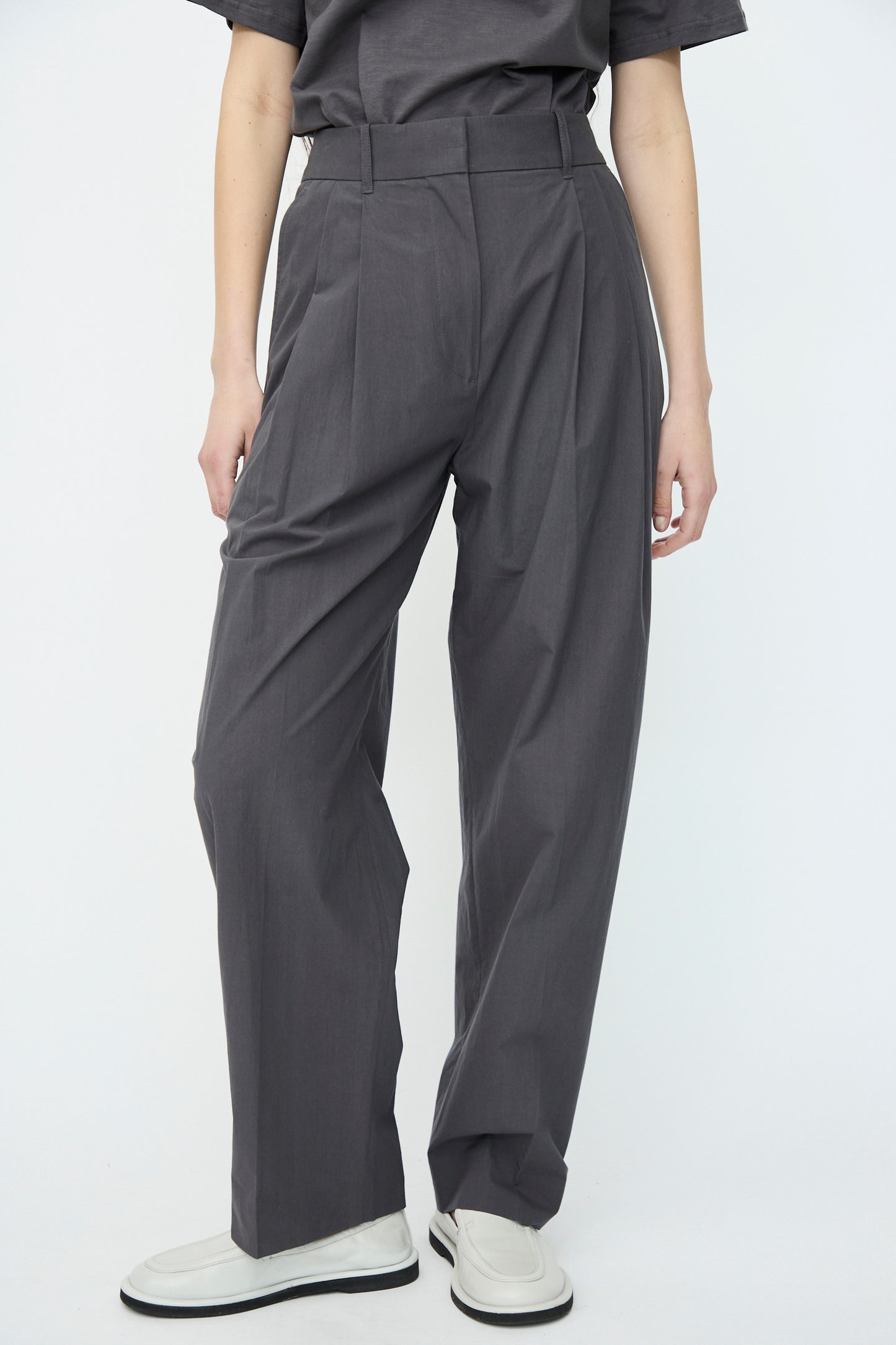 A person wearing Studio Nicholson's Typewriter Cotton Sperro Pant in Thunder and white shoes stands against a neutral background.