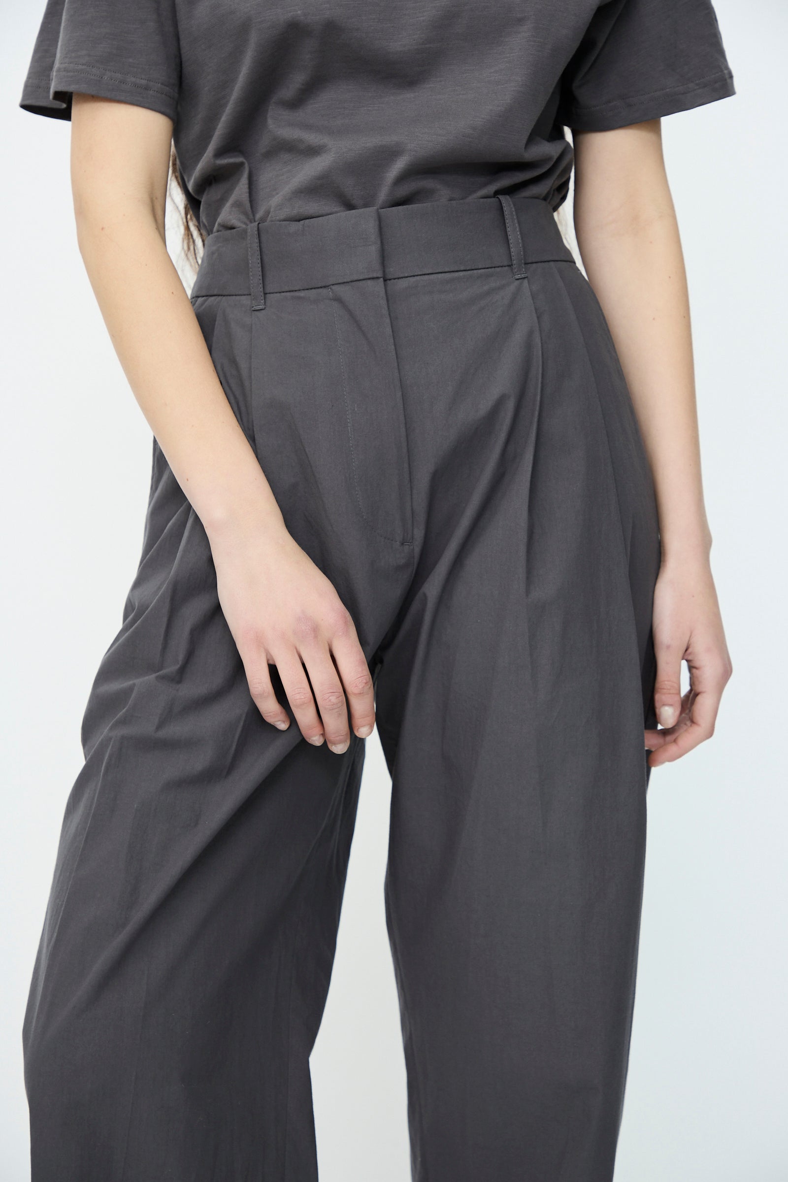 A person wearing Studio Nicholson's Typewriter Cotton Sperro Pant in Thunder—gray tailored high-waisted pants—paired with a relaxed fit t-shirt, stands with arms at their sides against a plain white background.