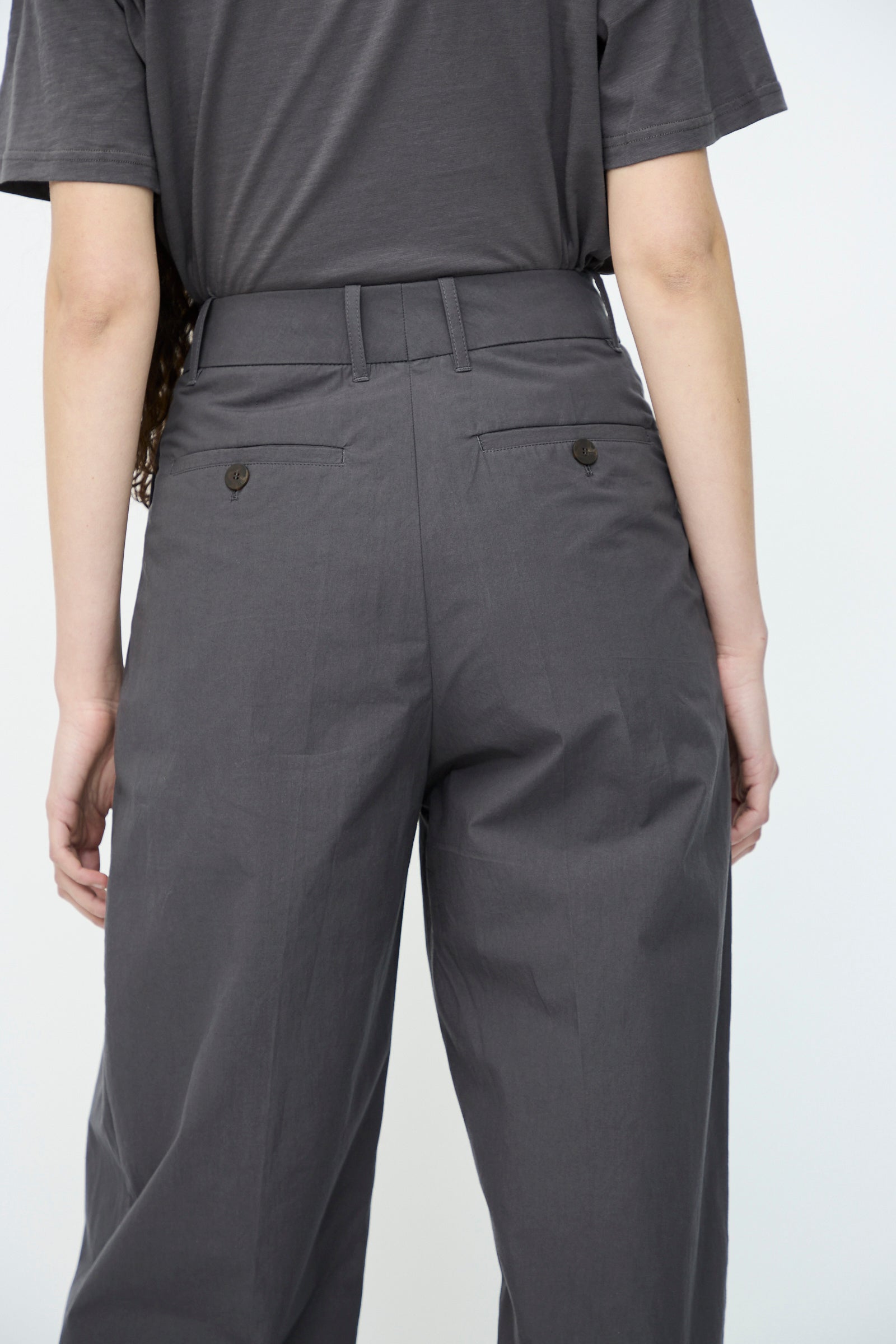 Back view of a person wearing Studio Nicholson's Typewriter Cotton Sperro Pant in Thunder, a relaxed-fit high-waisted design, paired with a matching short-sleeve shirt.