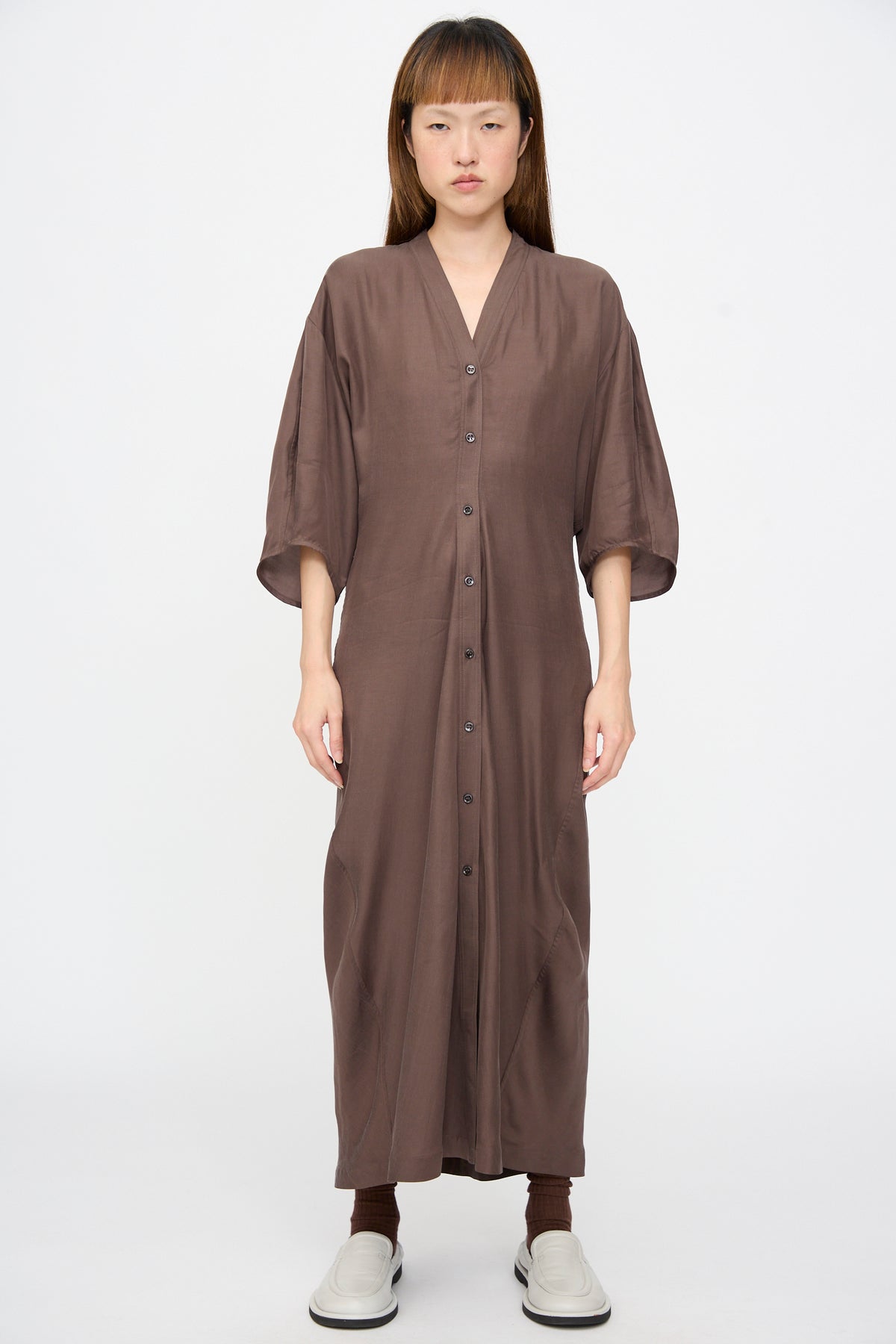 A person wearing a long-sleeved, button-front brown Yosha Dress in Porchini midi dress with a V-neckline, brown socks, and white loafers.
