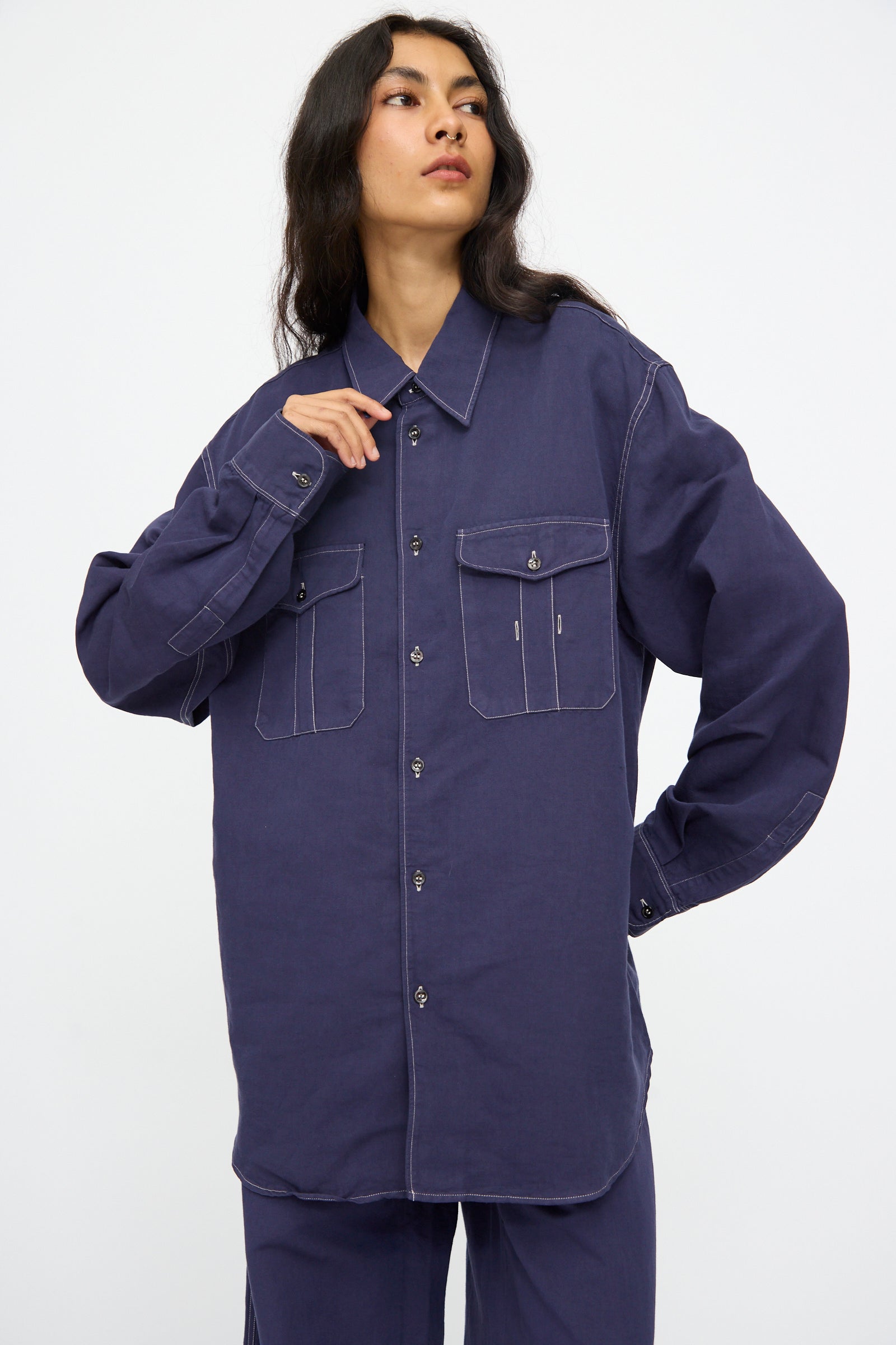 Model wears the Studio Nicholson Louro Utility Pocket Shirt in Indigo—an oversized, relaxed-fit linen shirt with long sleeves and two front pockets—shown against a plain white background.