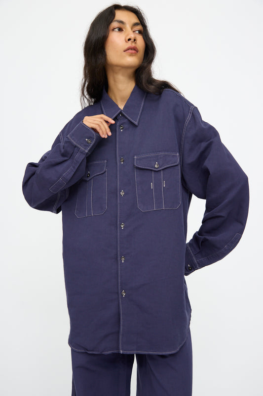 Model wears the Studio Nicholson Louro Utility Pocket Shirt in Indigo—an oversized, relaxed-fit linen shirt with long sleeves and two front pockets—shown against a plain white background.