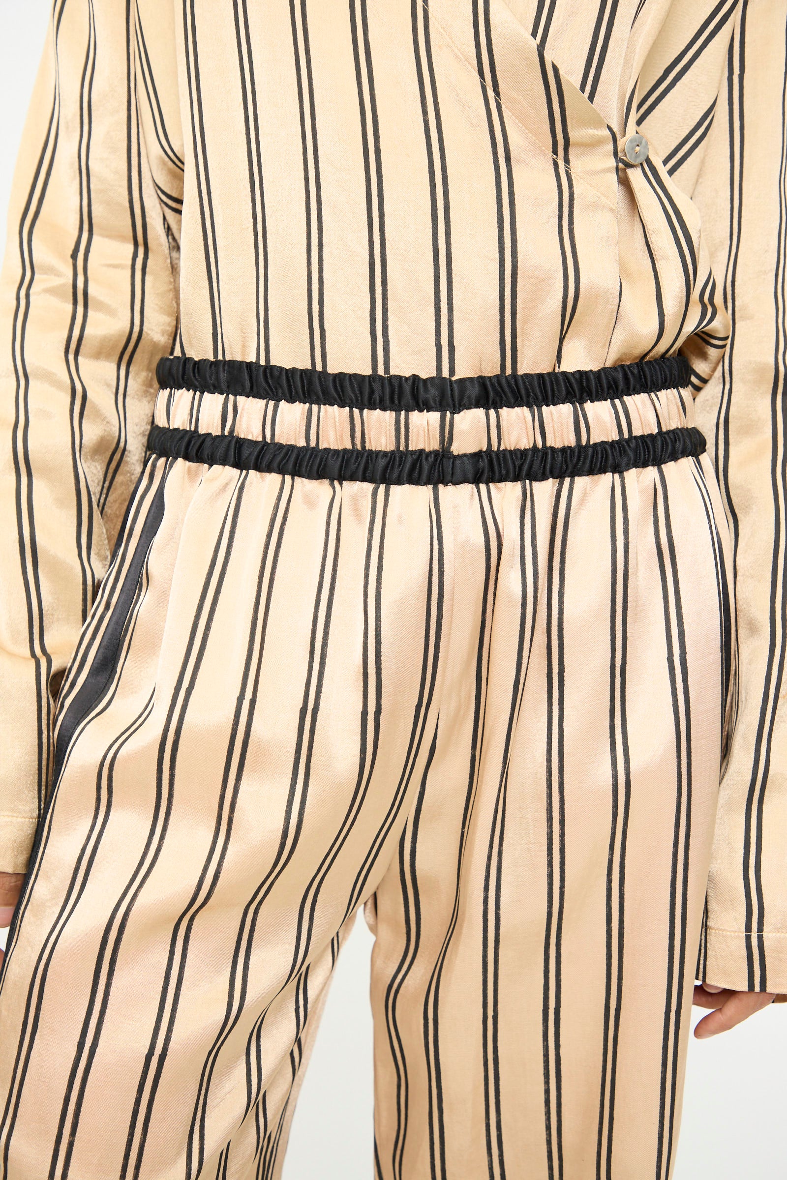A person wears the TIGRA TIGRA Block Printed Boxing Pant in Champagne and Black, featuring black vertical stripes and two black elastic waistbands, reminiscent of classic boxing styles. Only the torso and upper legs are visible. 