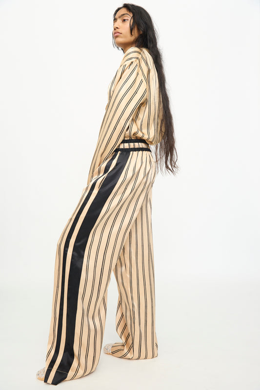 A person stands in profile against a plain white background, wearing TIGRA TIGRA’s Block Printed Boxing Pant in Champagne and Black—a loose-fitting silhouette inspired by classic boxing pants, crafted from silk mashroo with black vertical stripes and a black stripe down the side.