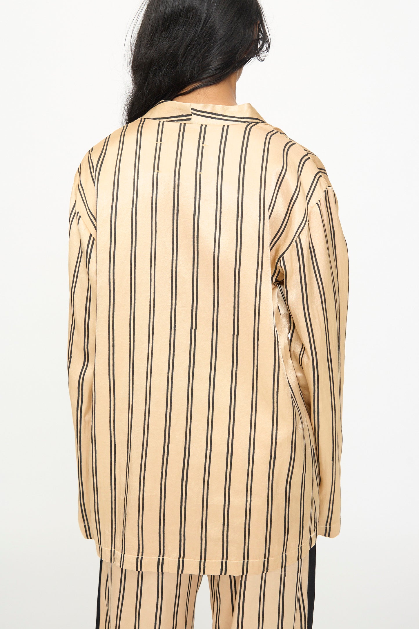 A person with long dark hair is photographed from the back wearing the TIGRA TIGRA Block Printed Striped Wrap Top in Champagne and Black.