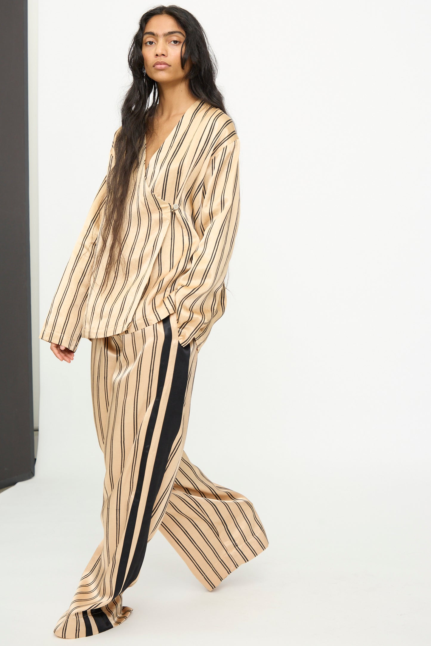 A model wears the TIGRA TIGRA Block Printed Striped Wrap Top in Champagne and Black, paired with matching wide-leg pants, standing against a plain white background.