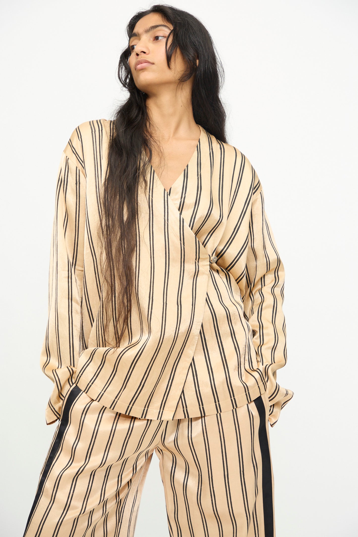 A model is wearing the TIGRA TIGRA Block Printed Striped Wrap Top in Champagne and Black, styled with matching pants, against a plain white background.