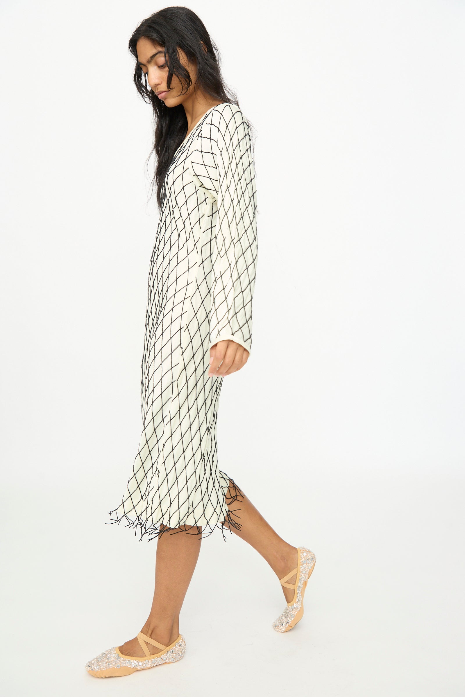 A woman wearing the TIGRA TIGRA Off the Shoulder Dress in pale yellow adorned with black glass beads and beige shoes, standing against a plain white background.