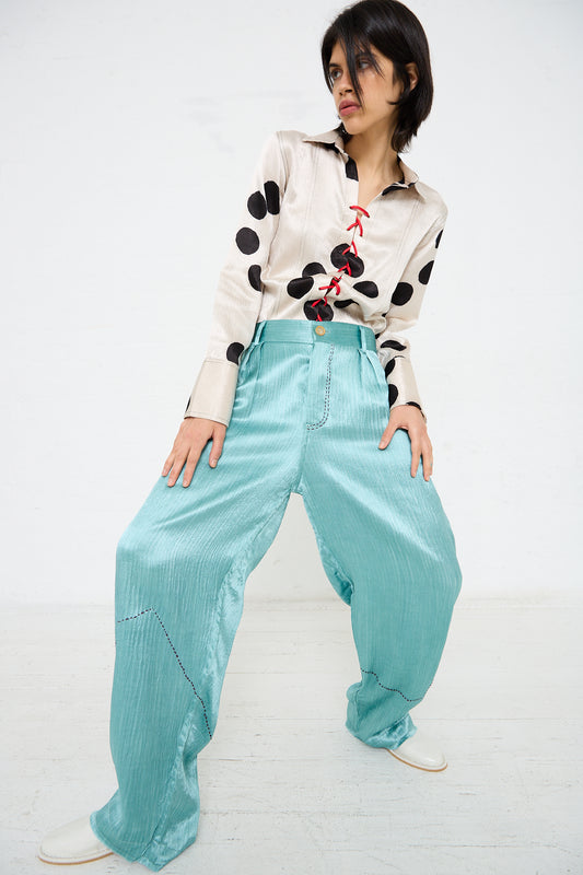 Person posing in a beige shirt with large black polka dots, blue high-waisted wide-leg Silk Mashroo Kantha Cargo Pant in Teal by TIGRA TIGRA, and white shoes, standing against a plain white background.