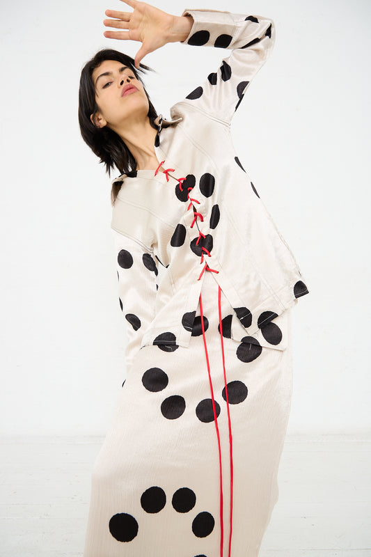 A person wearing a Silk Mashroo Lace Up Shirt in White by TIGRA TIGRA with hand clamp dyed moon dots and red lace detail strikes a pose against a plain white background.