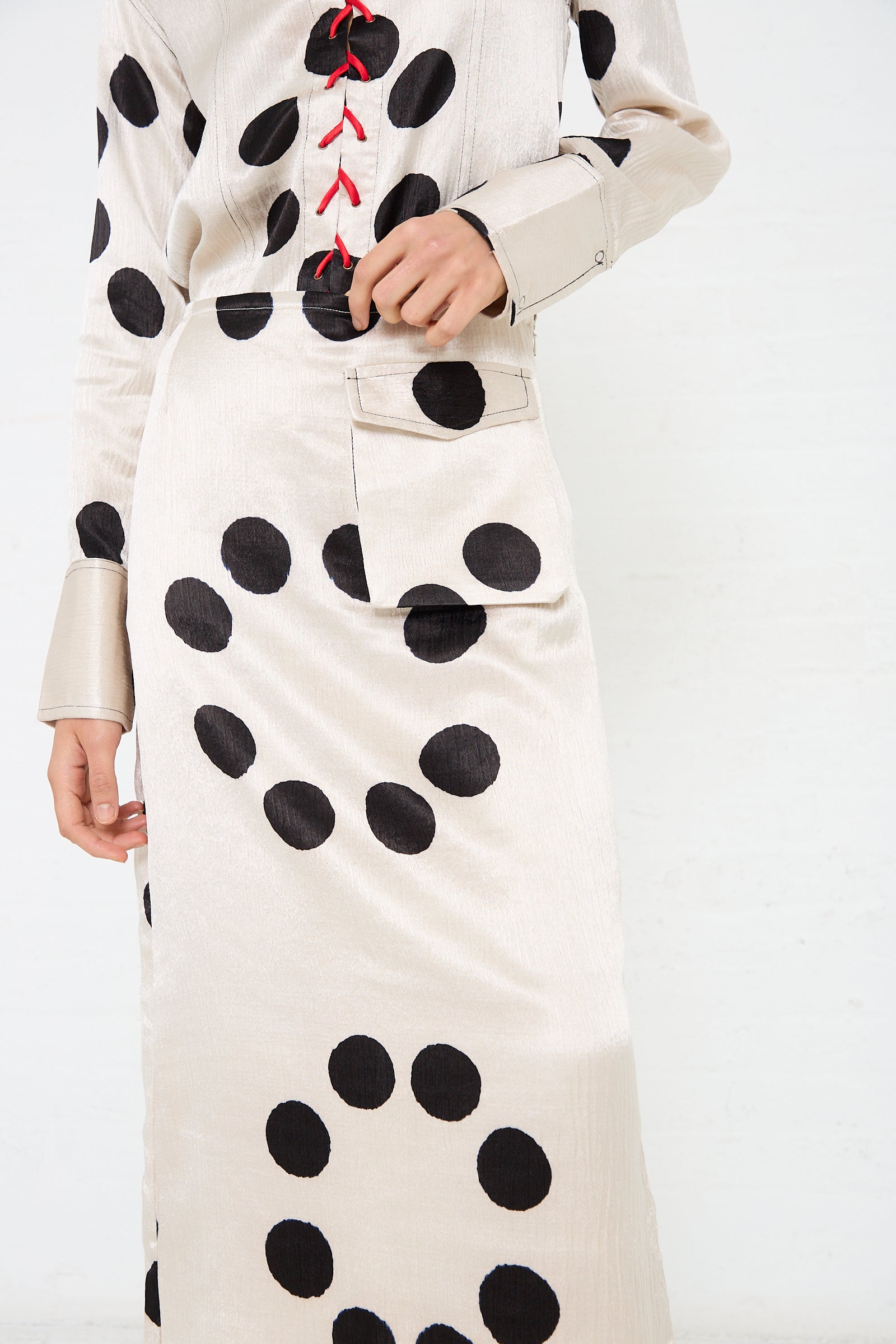 Person wearing a long, light-colored dress with large black polka dots and red lacing detail on the front, featuring a handwoven Silk Mashroo Midi Skirt by TIGRA TIGRA with visible pocket and subtle contrast topstitching.