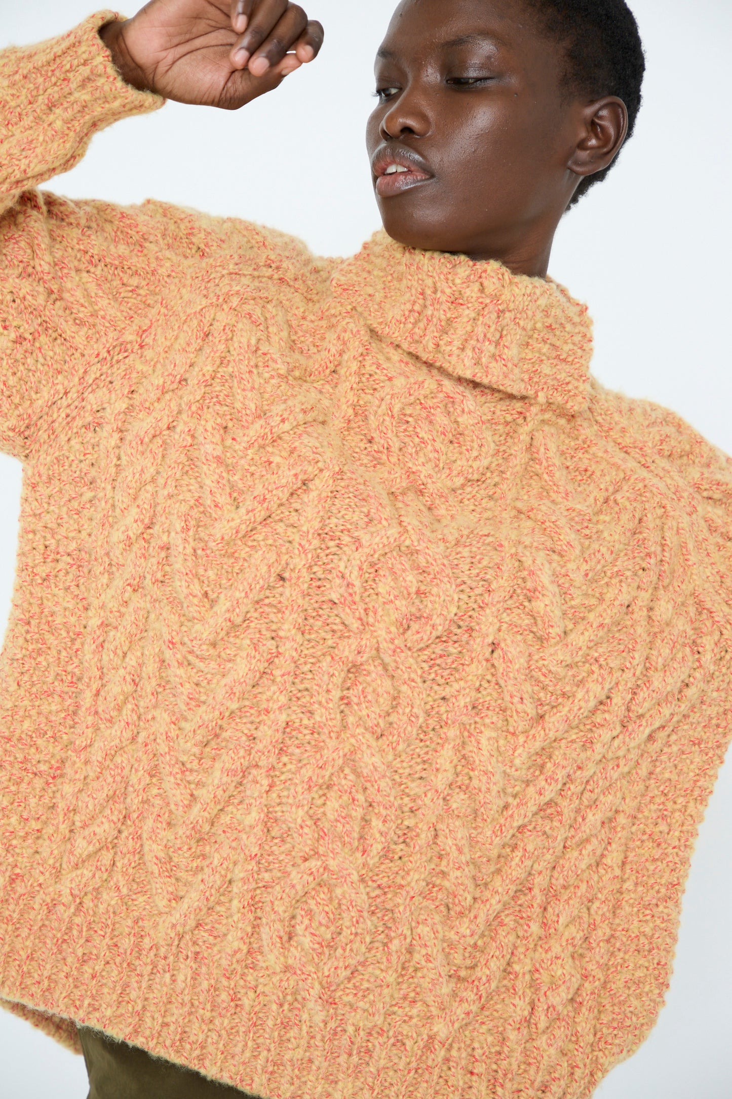 A person is wearing a yellow cable knit pullover from TOGA ARCHIVES with one arm raised against a plain background.