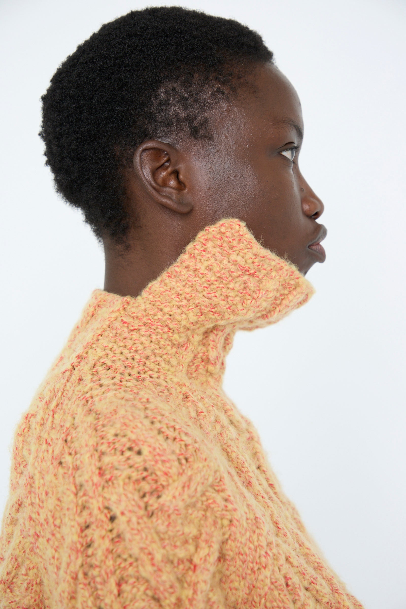 A person in profile is wearing a textured, yellow cable knit pullover from TOGA ARCHIVES against a plain background.