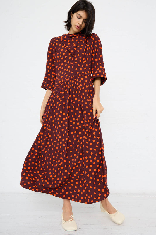 A person stands against a plain white background wearing the Dot Print Dress in Red by TOGA ARCHIVES, complemented by cream-colored shoes. The long-sleeved, ankle-length outfit, likely made of soft rayon, exudes both comfort and style.