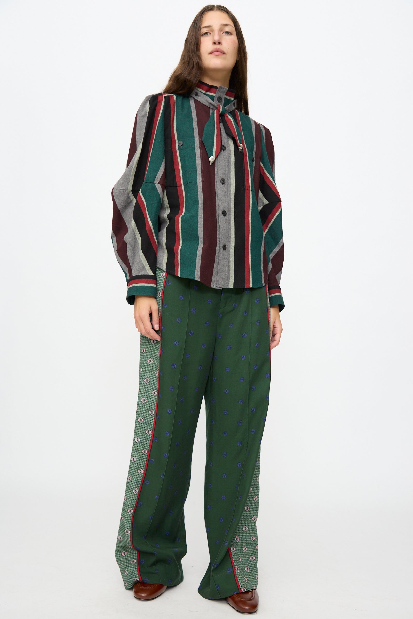 Wearing the TOGA ARCHIVES Flannel Striped Shirt in Green, paired with a necktie and loose green patterned pants, this person stands against a plain white background.
