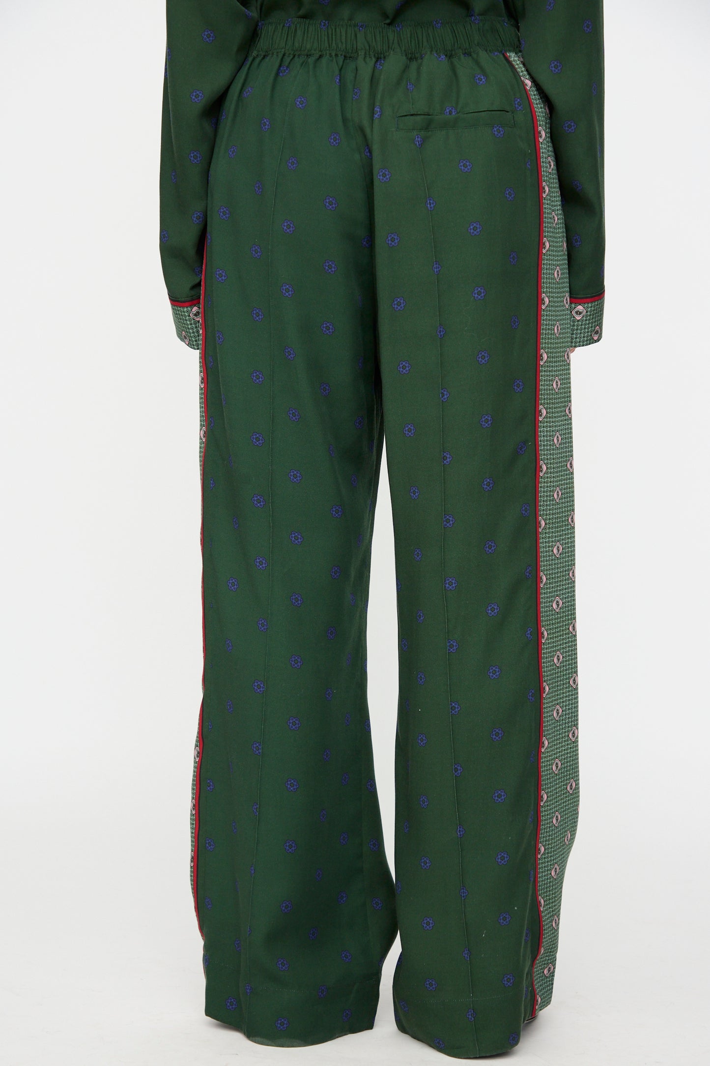 Model wears the TOGA ARCHIVES Inner Print Drawstring Pant in Green, featuring a green cupra fabric with small blue patterns, red side piping, and a contrasting patterned side panel; back view shown from waist to feet.