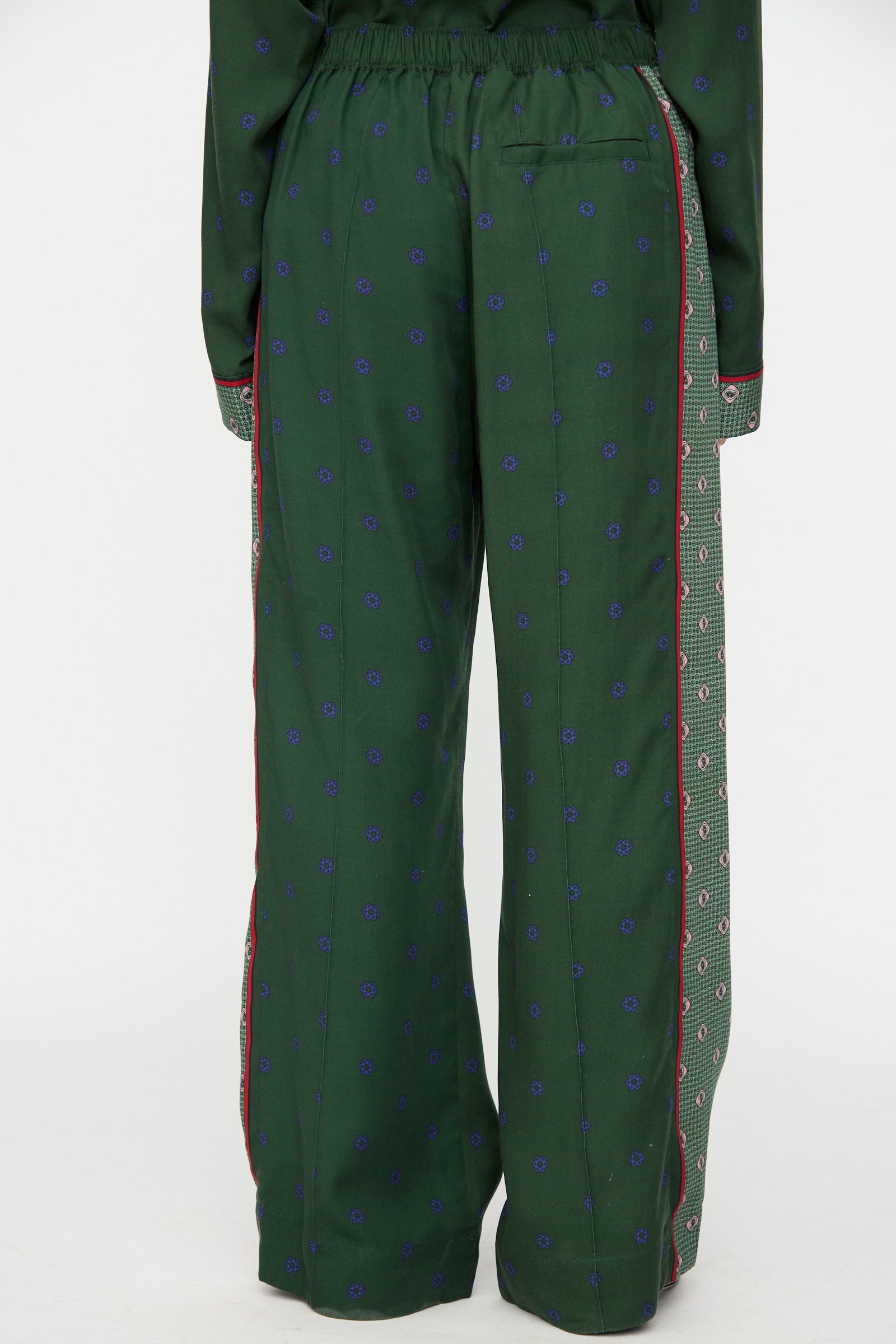 Model wears the TOGA ARCHIVES Inner Print Drawstring Pant in Green, featuring a green cupra fabric with small blue patterns, red side piping, and a contrasting patterned side panel; back view shown from waist to feet.