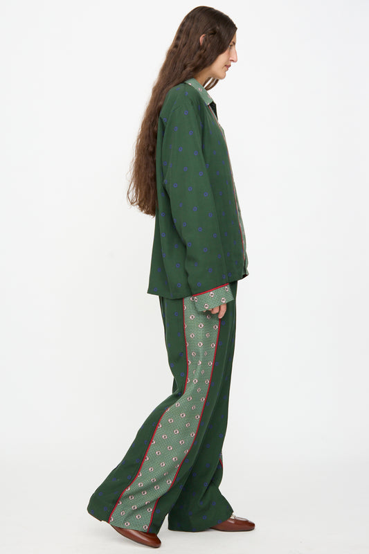 Wearing TOGA ARCHIVES Inner Print Drawstring Pant in Green, a person with long hair stands in profile against a plain white background. They pair the loose-fitting green patterned pants with a matching suit and brown shoes.