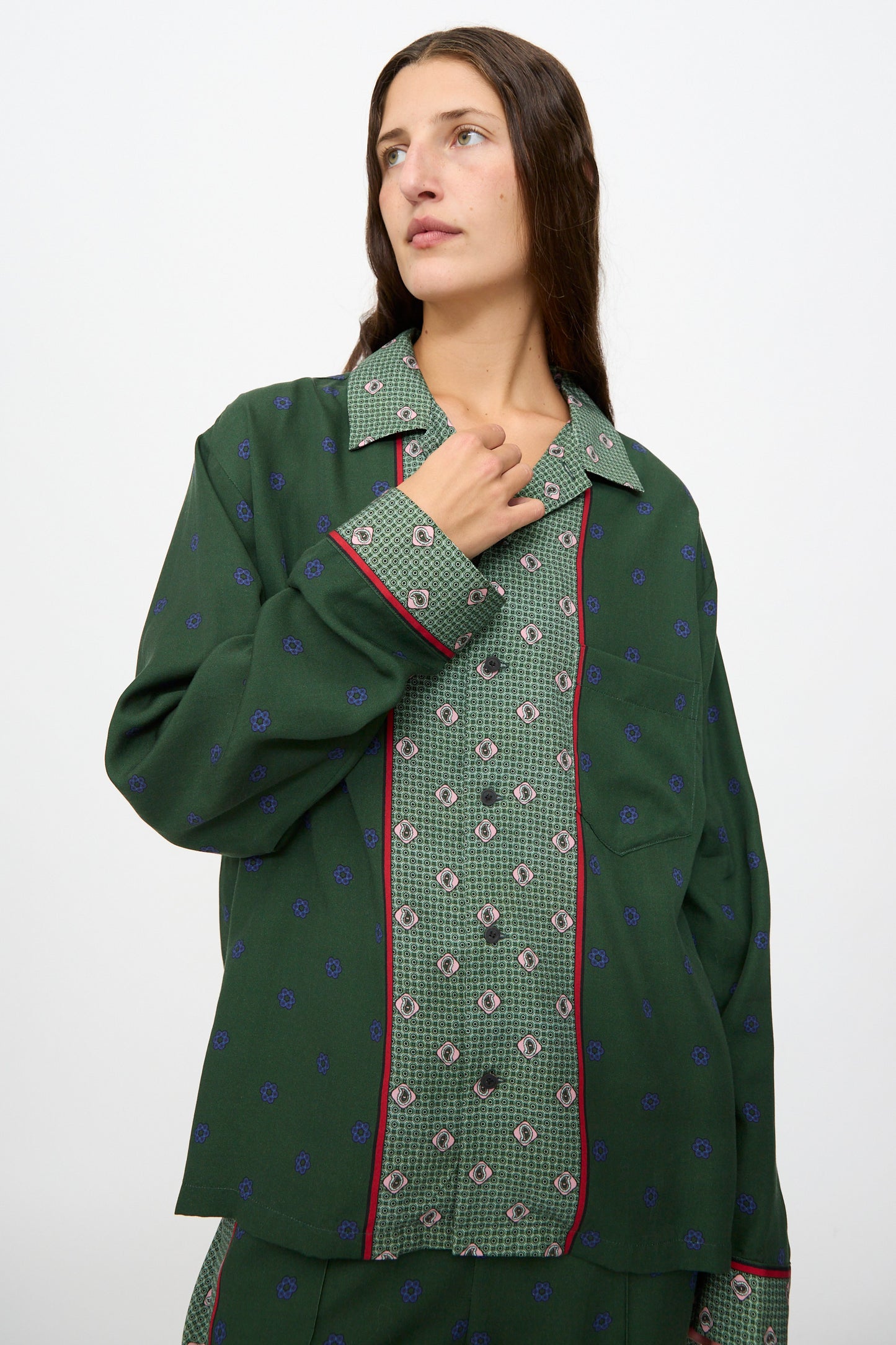 A woman wearing the TOGA ARCHIVES Inner Print Long Sleeve Shirt in Green with matching pants stands against a plain white background, gazing slightly to the side.