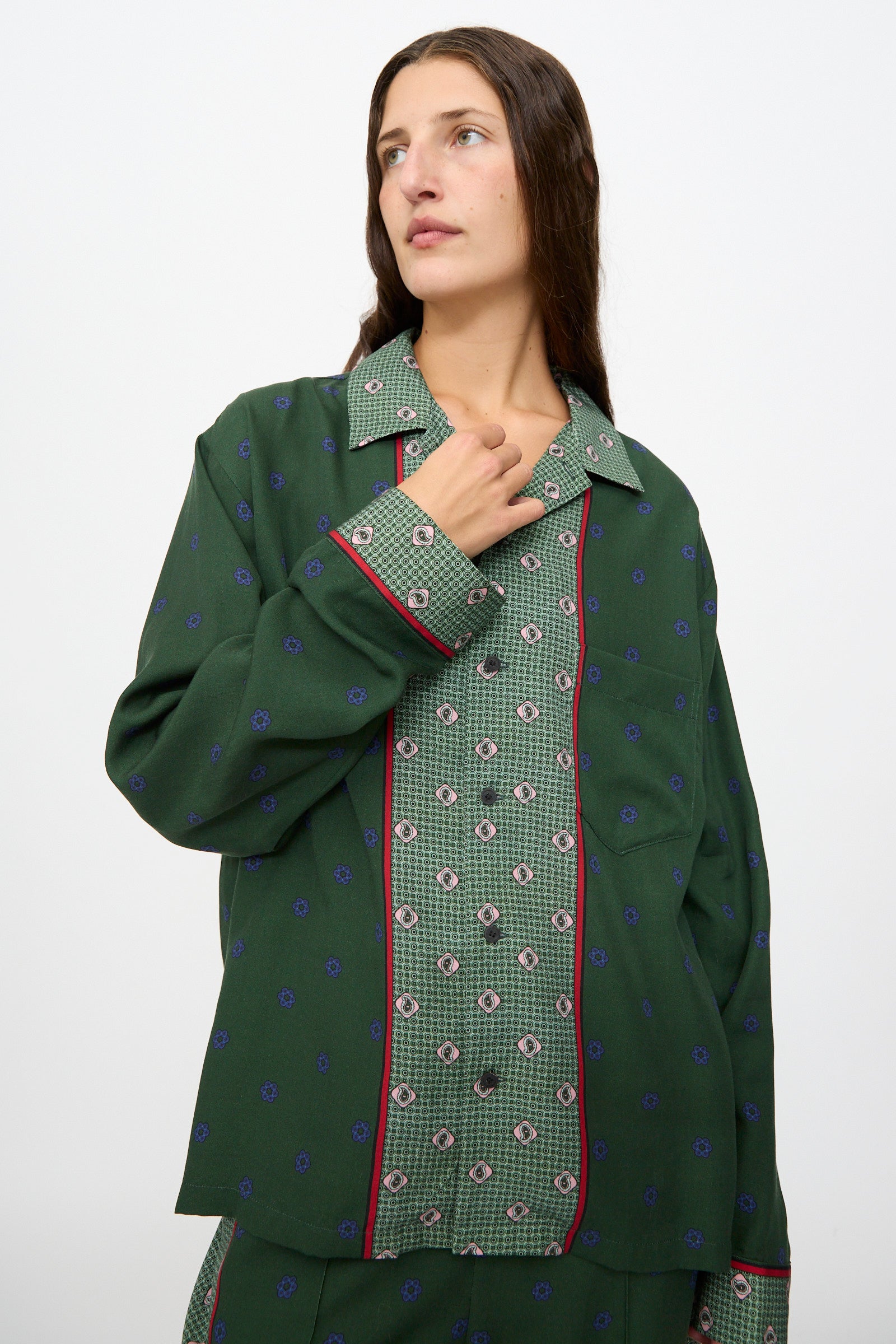 A woman wearing the TOGA ARCHIVES Inner Print Long Sleeve Shirt in Green with matching pants stands against a plain white background, gazing slightly to the side.