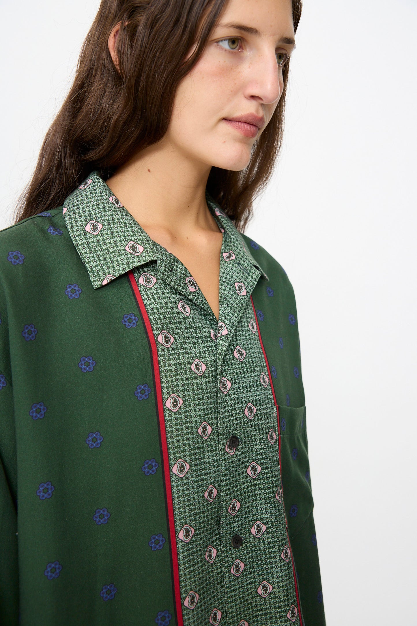 A person with long brown hair wears the TOGA ARCHIVES Inner Print Long Sleeve Shirt in Green, featuring blue and red accents, while looking away from the camera against a plain background.