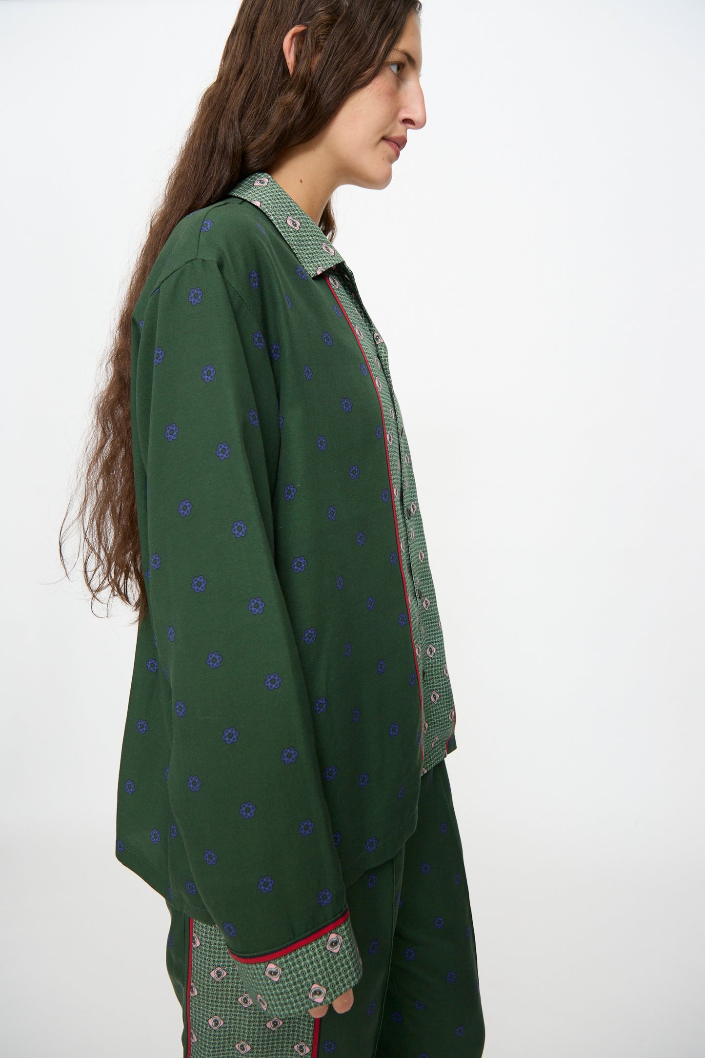 A person with long brown hair is standing in profile against a plain white background, wearing the TOGA ARCHIVES Inner Print Long Sleeve Shirt in Green with matching pants.