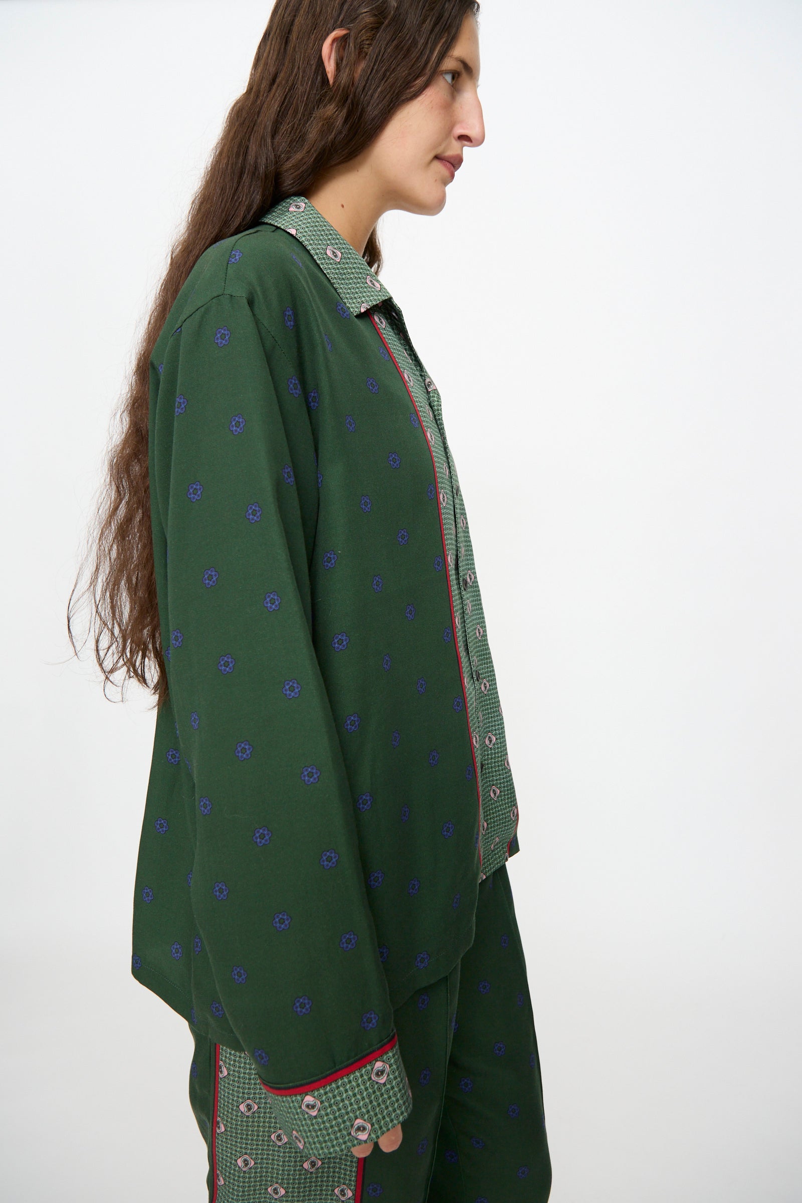 A person with long brown hair is standing in profile against a plain white background, wearing the TOGA ARCHIVES Inner Print Long Sleeve Shirt in Green with matching pants.