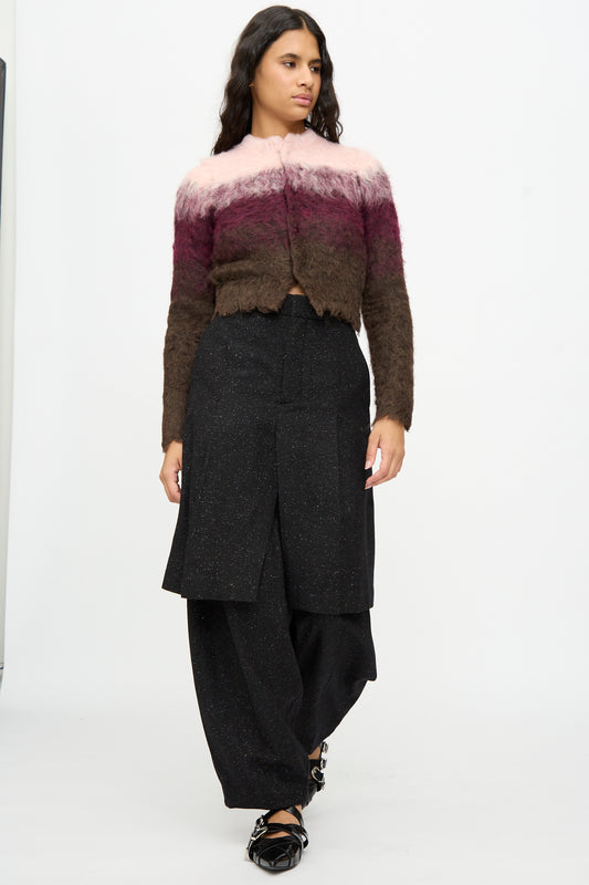A woman stands in a studio wearing a fuzzy ombre cardigan in pink, brown, and burgundy tones paired with TOGA ARCHIVES Layered Trousers in Black and black flat shoes.