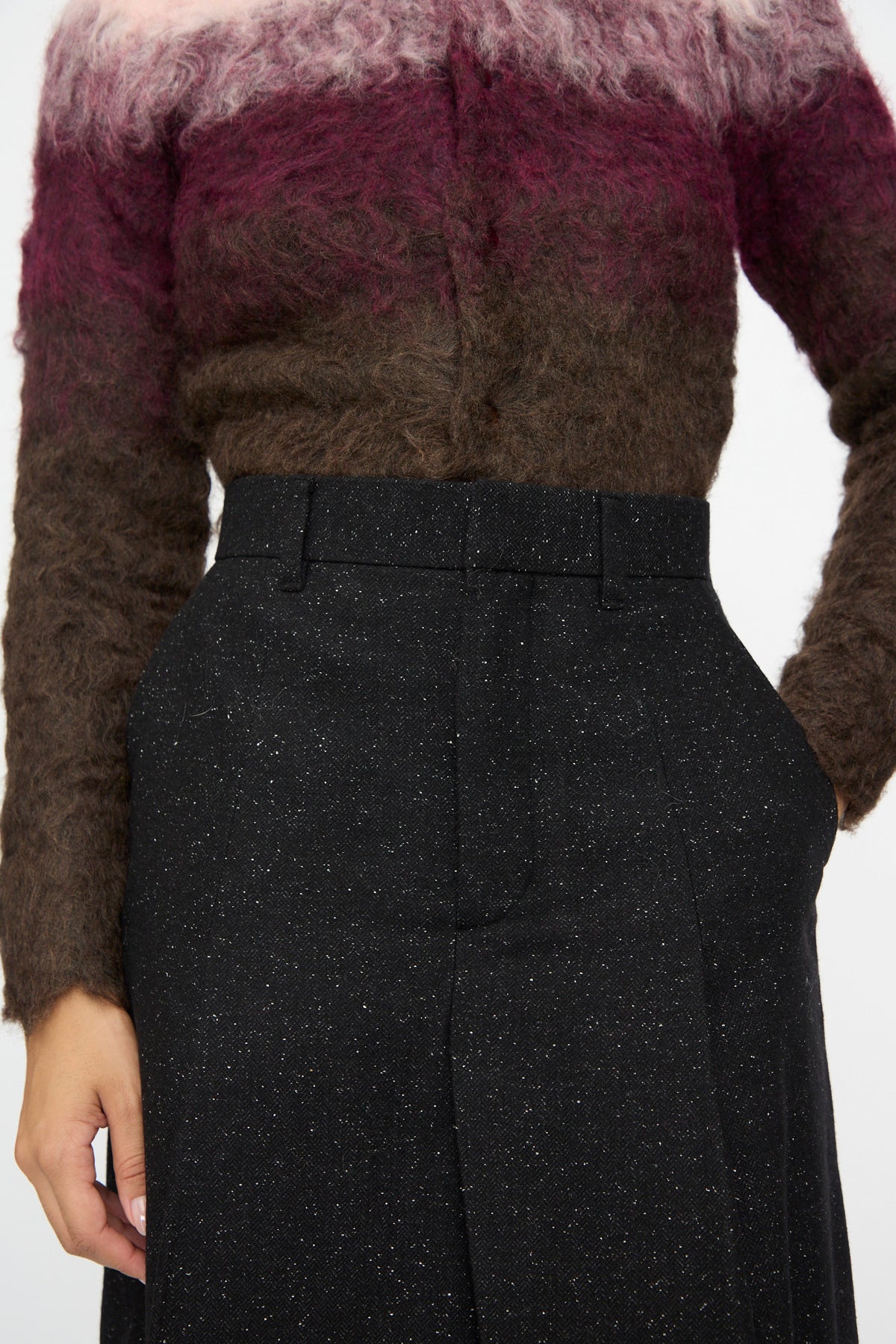 A person wears a fuzzy, gradient sweater in pink and brown tones paired with TOGA ARCHIVES Layered Trousers in Black. Only the torso and part of the left hand are visible. The unique layered design of the trousers adds visual interest to this modern ensemble.