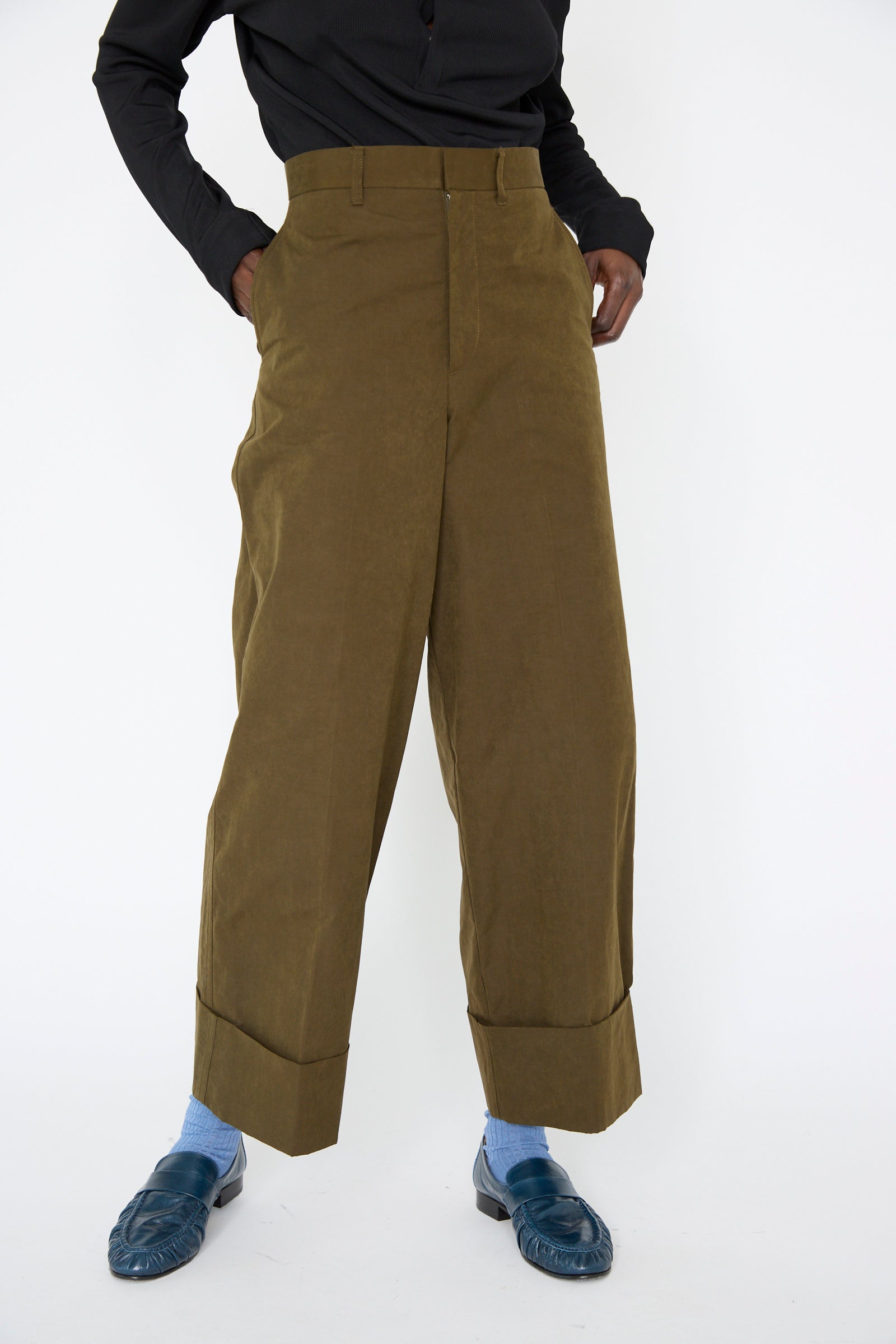 A person is wearing the Polyester Cotton Pant in Khaki by TOGA ARCHIVES, complemented by a black top, blue socks, and blue loafers.