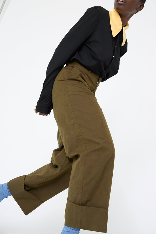 A person in a black long-sleeve shirt with a large yellow collar, wearing TOGA ARCHIVES Polyester Cotton Pant in khaki and blue socks, leans forward slightly against a white background.