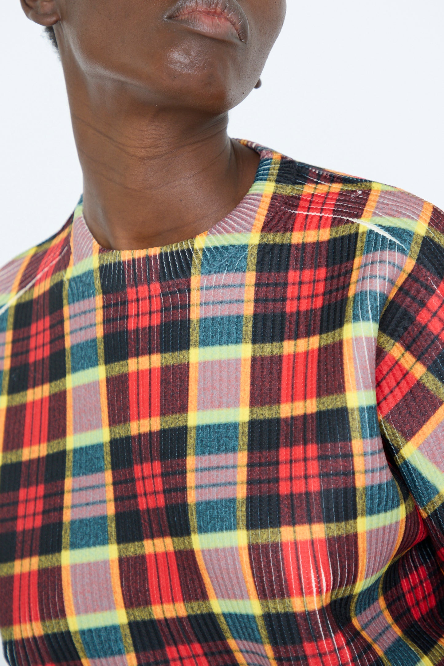 A person wearing the Print Knit Pullover in Red by TOGA ARCHIVES, a vibrant combination of red, yellow, green, and black plaid patterns. 