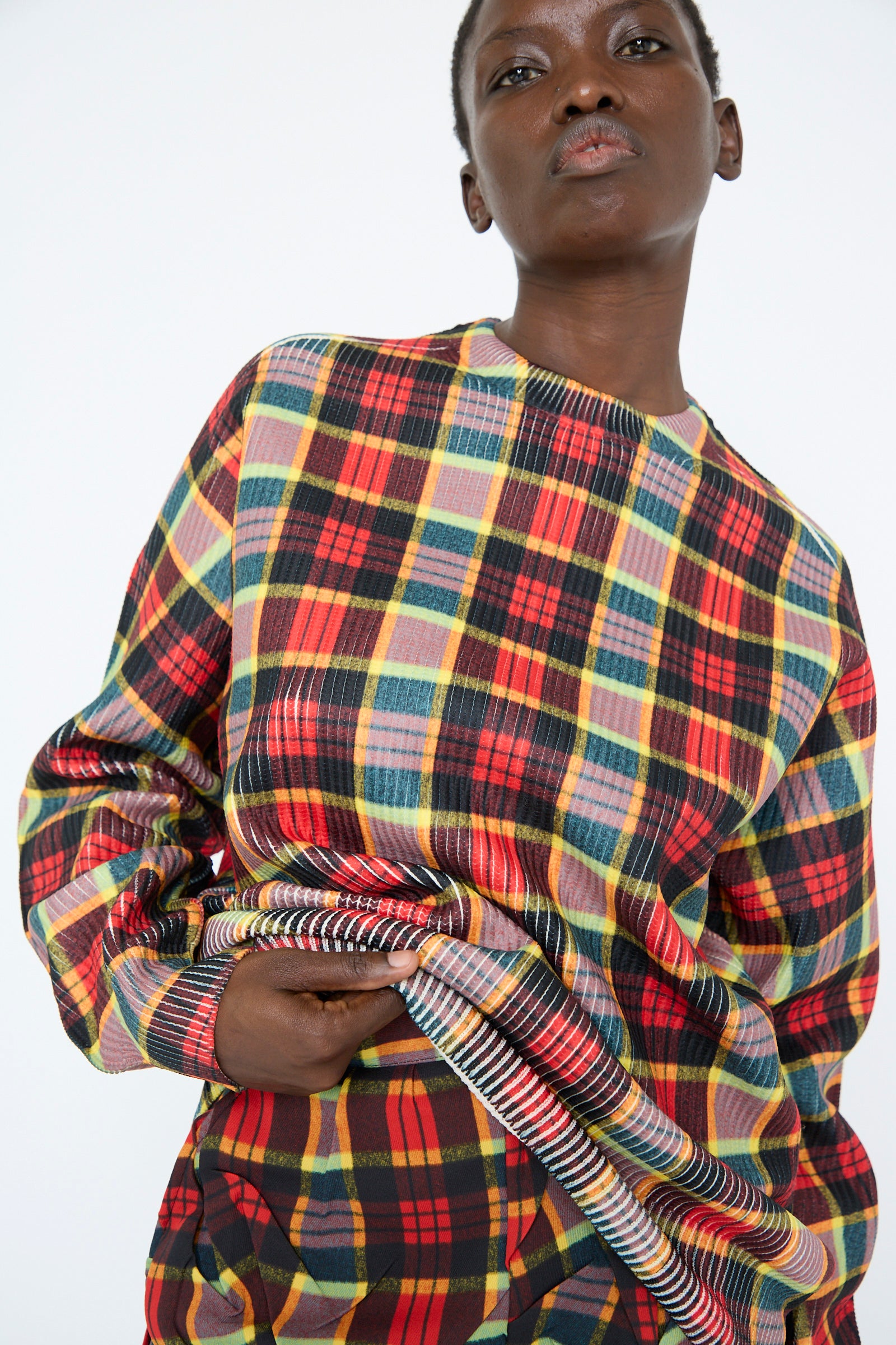 A person wearing the TOGA ARCHIVES Print Knit Pullover in Red with their hand holding up the hem, against a plain white background.