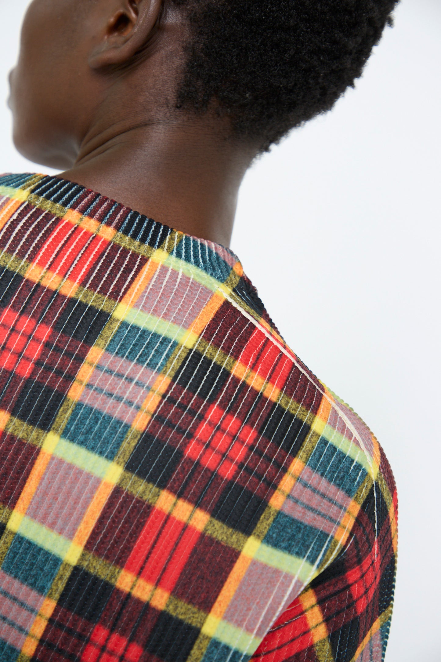 A person is wearing the Print Knit Pullover in Red by TOGA ARCHIVES, featuring a colorful plaid pattern, a ribbed texture, and long sleeves, shown from the back.