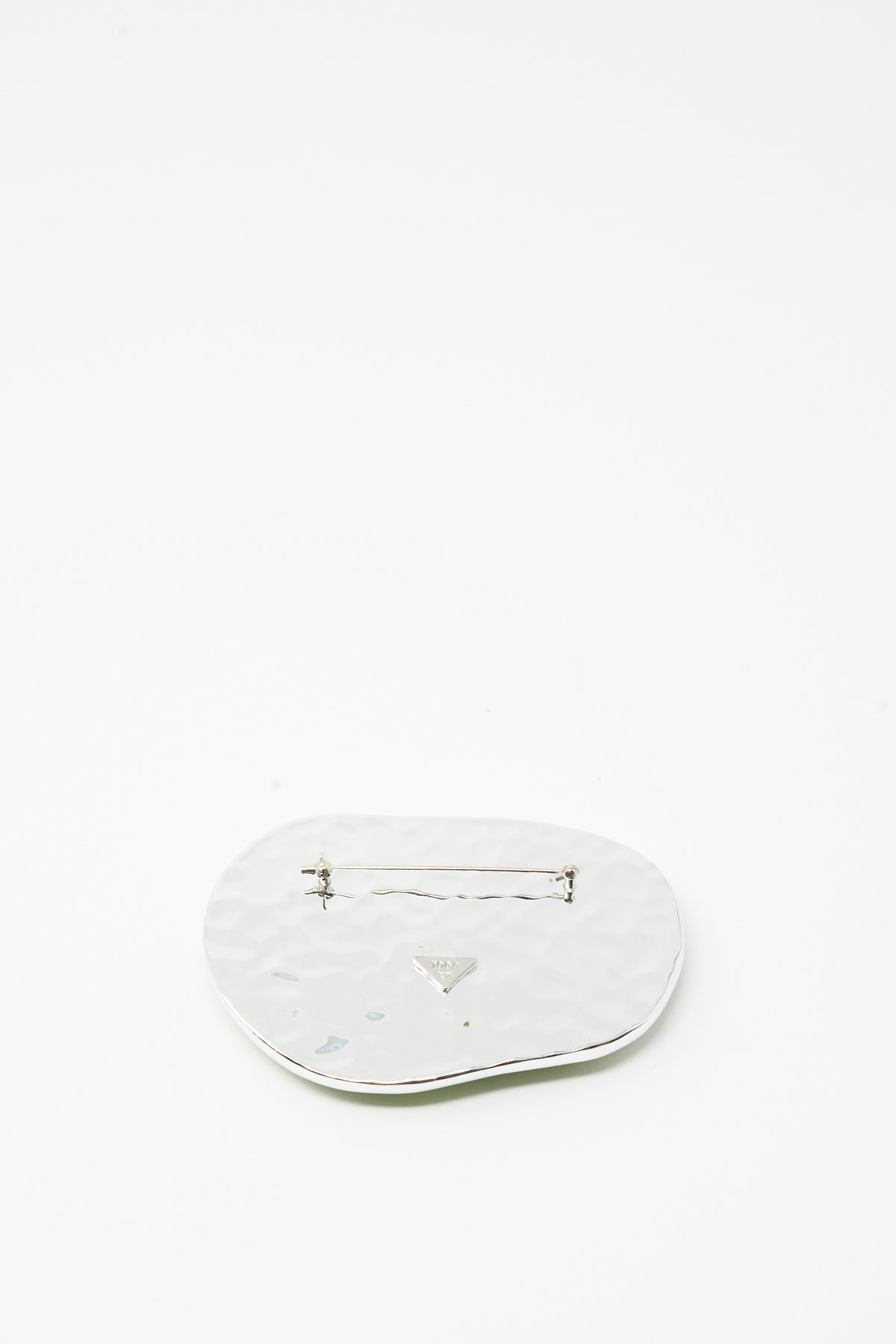 A light green, round wave-shaped brooch by TOGA ARCHIVES, crafted from silver-tone brass with a textured surface and an irregular form. It features a secure back clasp and is artfully displayed on a plain white background. Expertly made in Japan, this piece is reminiscent of a resin brooch.