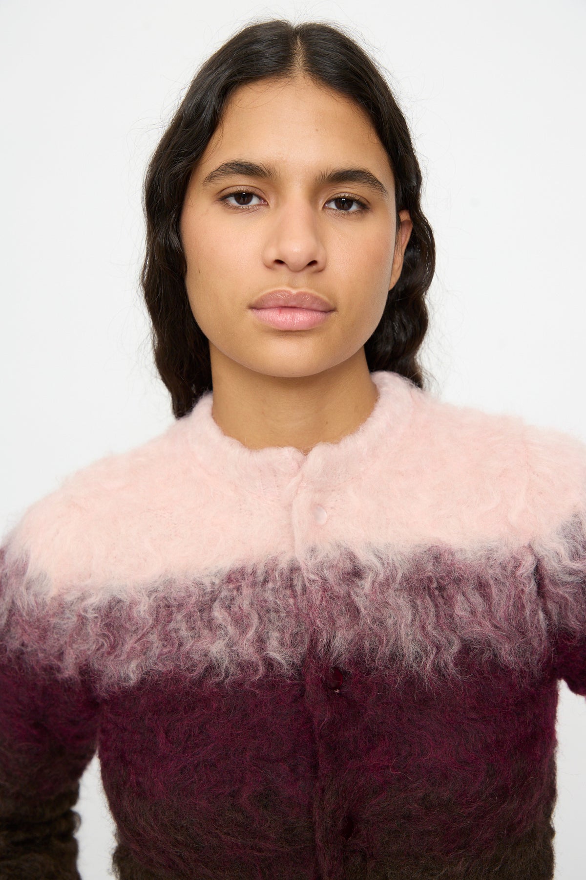 A person with long dark hair models the TOGA ARCHIVES Shaggy Knit Cardigan in Pink, which features pink, purple, and dark brown sections, standing against a plain white background.