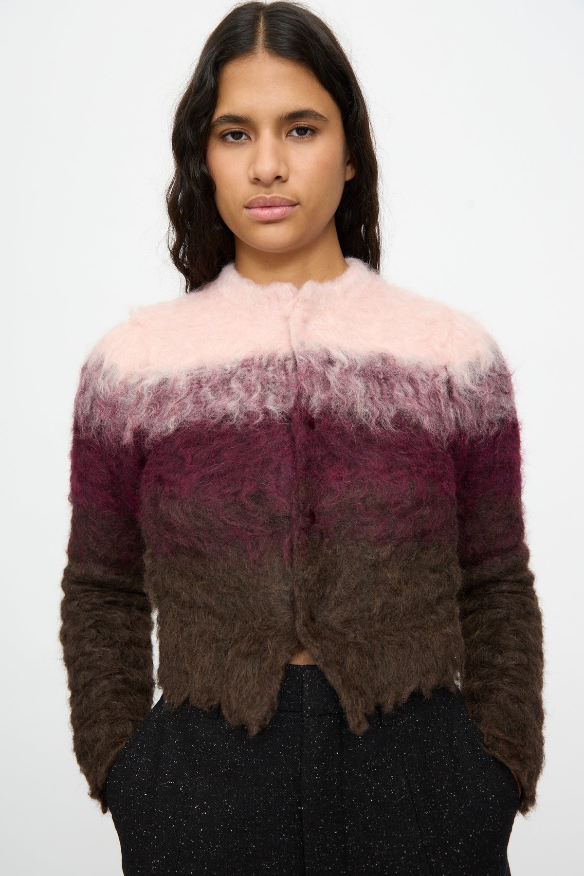 A person is wearing the TOGA ARCHIVES Shaggy Knit Cardigan in Pink, featuring ombre shades of pink, burgundy, and brown, and is standing against a plain white background.